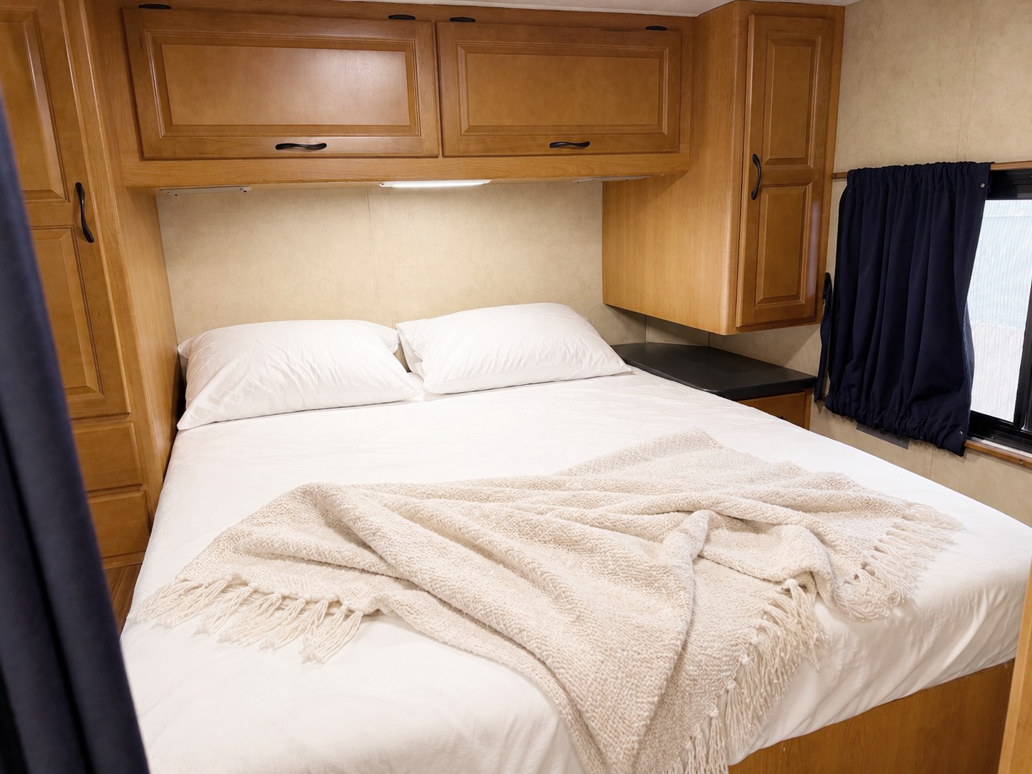 Experience comfort in this RV rental bedroom with a neatly made white bed, pillows, a fringed throw, and wood cabinetry.. Thor Majestic 2014