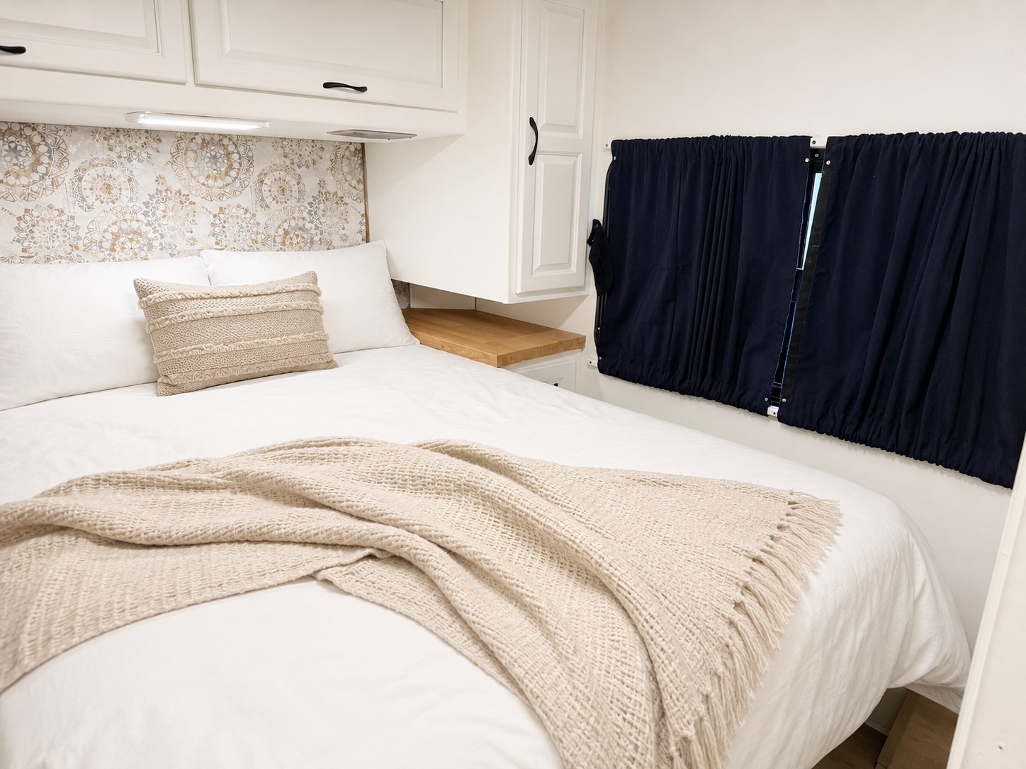 Cozy, renovated RV rental bedroom: white bedding, patterned headboard, wood accents, and navy blackout curtains.. Thor Majestic 2012