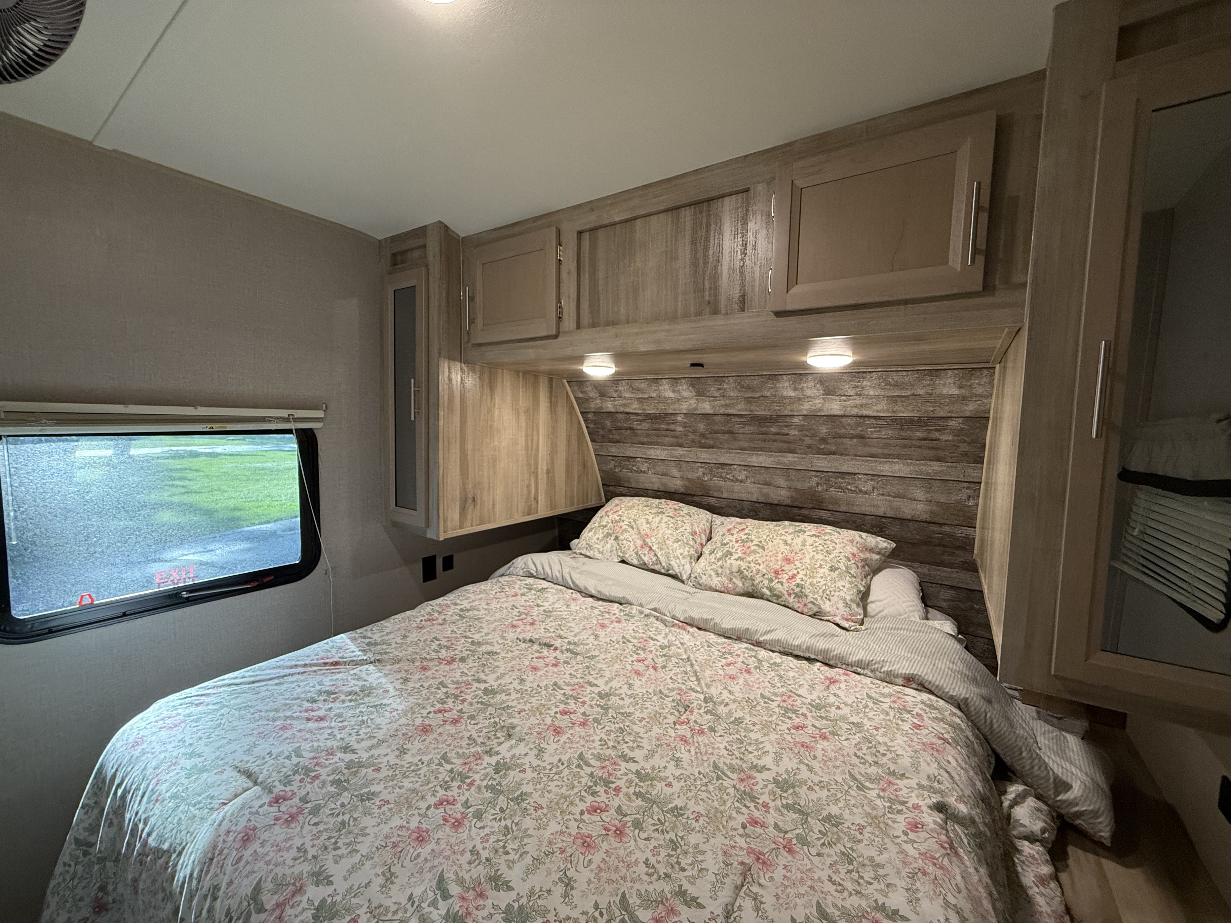 Cozy RV rental bedroom with floral bedding, wooden cabinets, and window view. Ideal for your next adventure.. Forest River Coachmen Catalina Legacy 2021