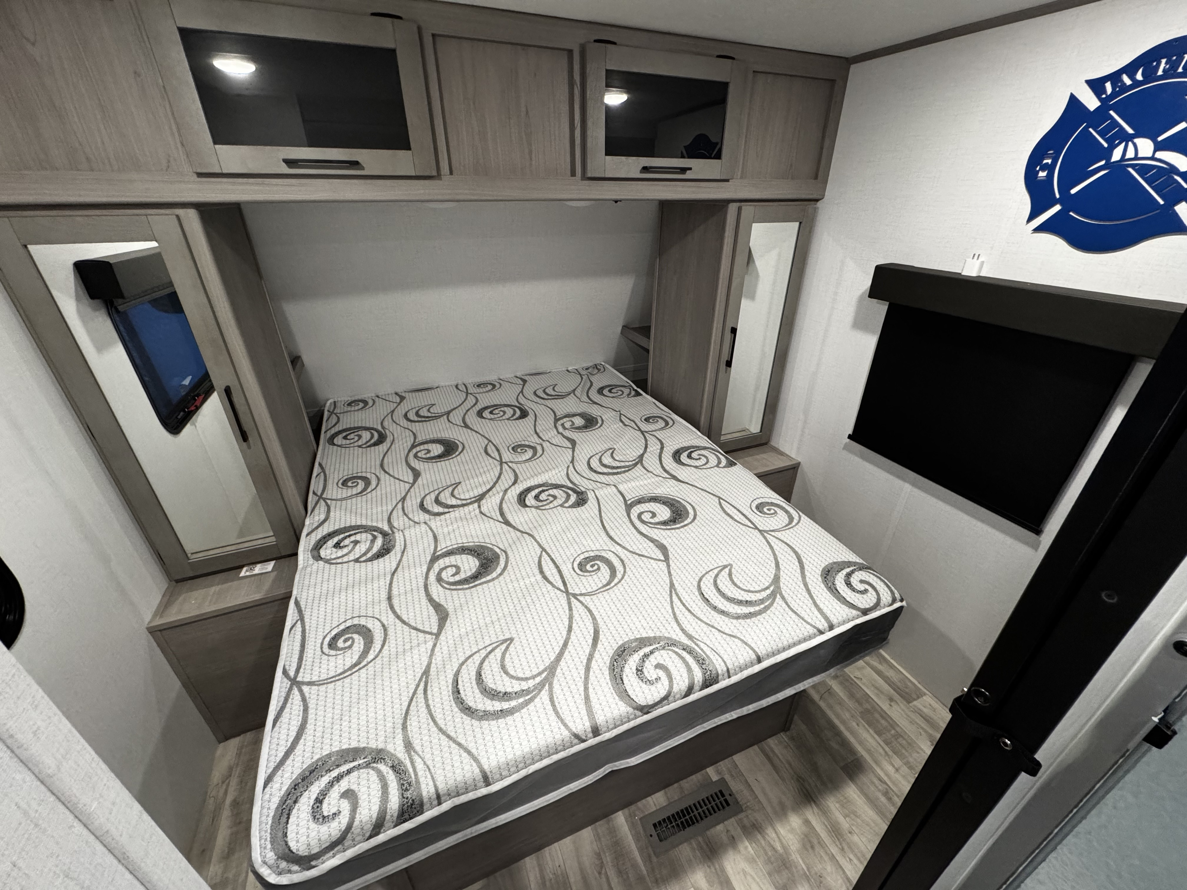 This RV rental bedroom features a bed with a patterned mattress, overhead cabinets, mirrored wardrobes, and a blackout window shade.. Dutchmen Kodiak Ultra Lite 2024