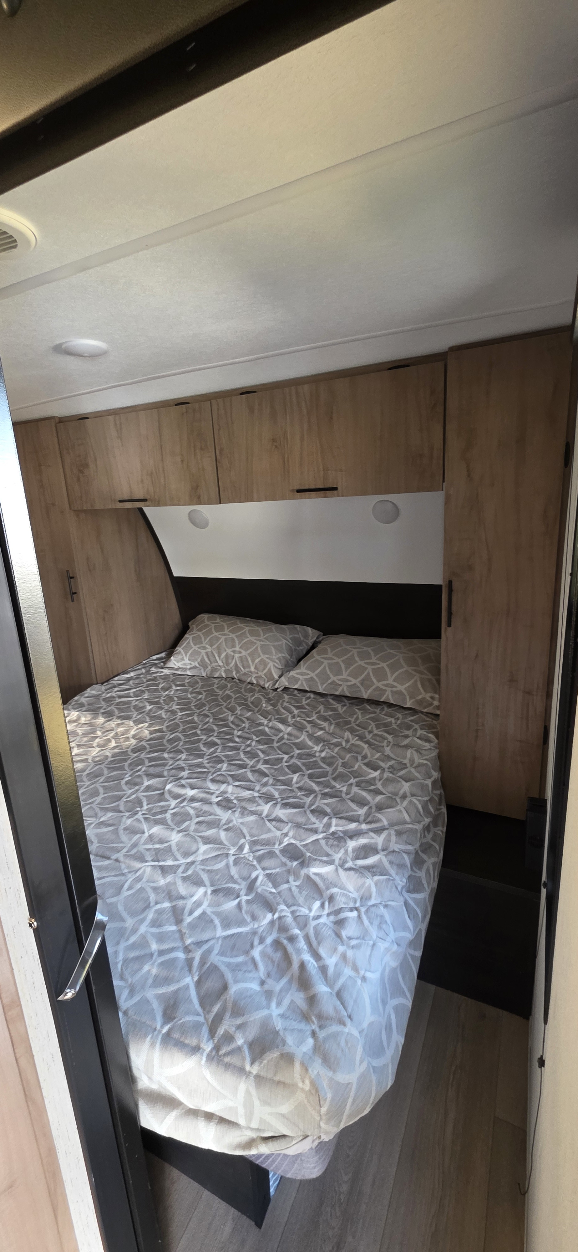 Cozy RV rental bedroom with a comfy bed, overhead cabinets, and dark headboard. A compact yet inviting sleeping area.. Forest River Cherokee Grey Wolf 2025