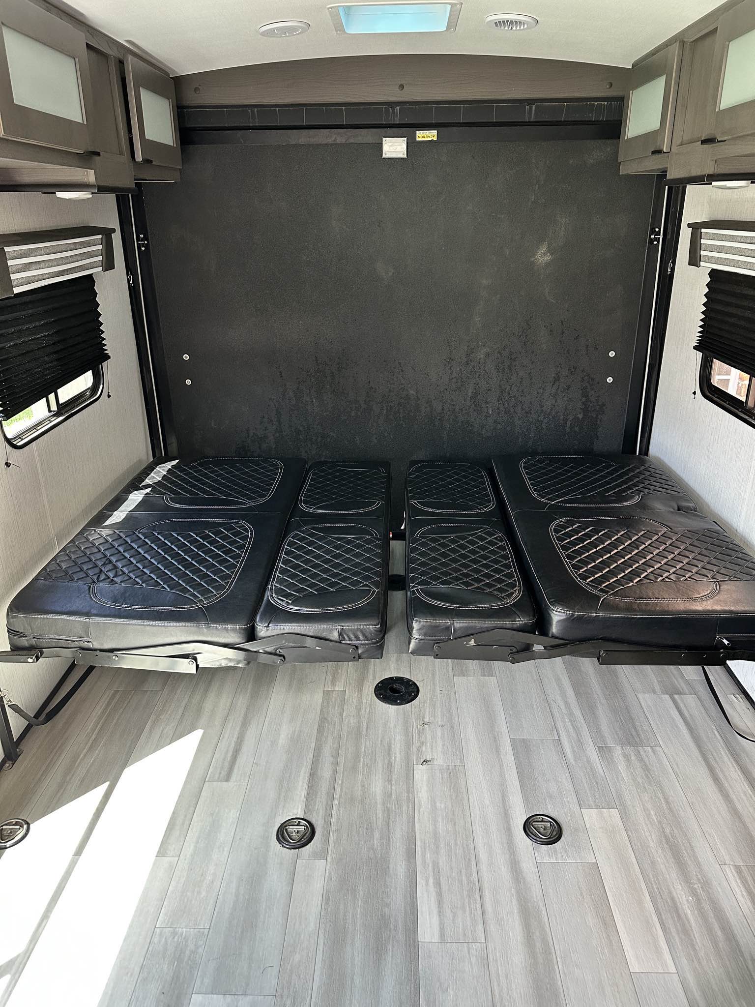 RV rental interior features black quilted fold-down beds, gray wood-look floor with tie-downs, and overhead cabinets.. Cruiser Rv Corp MPG 2023