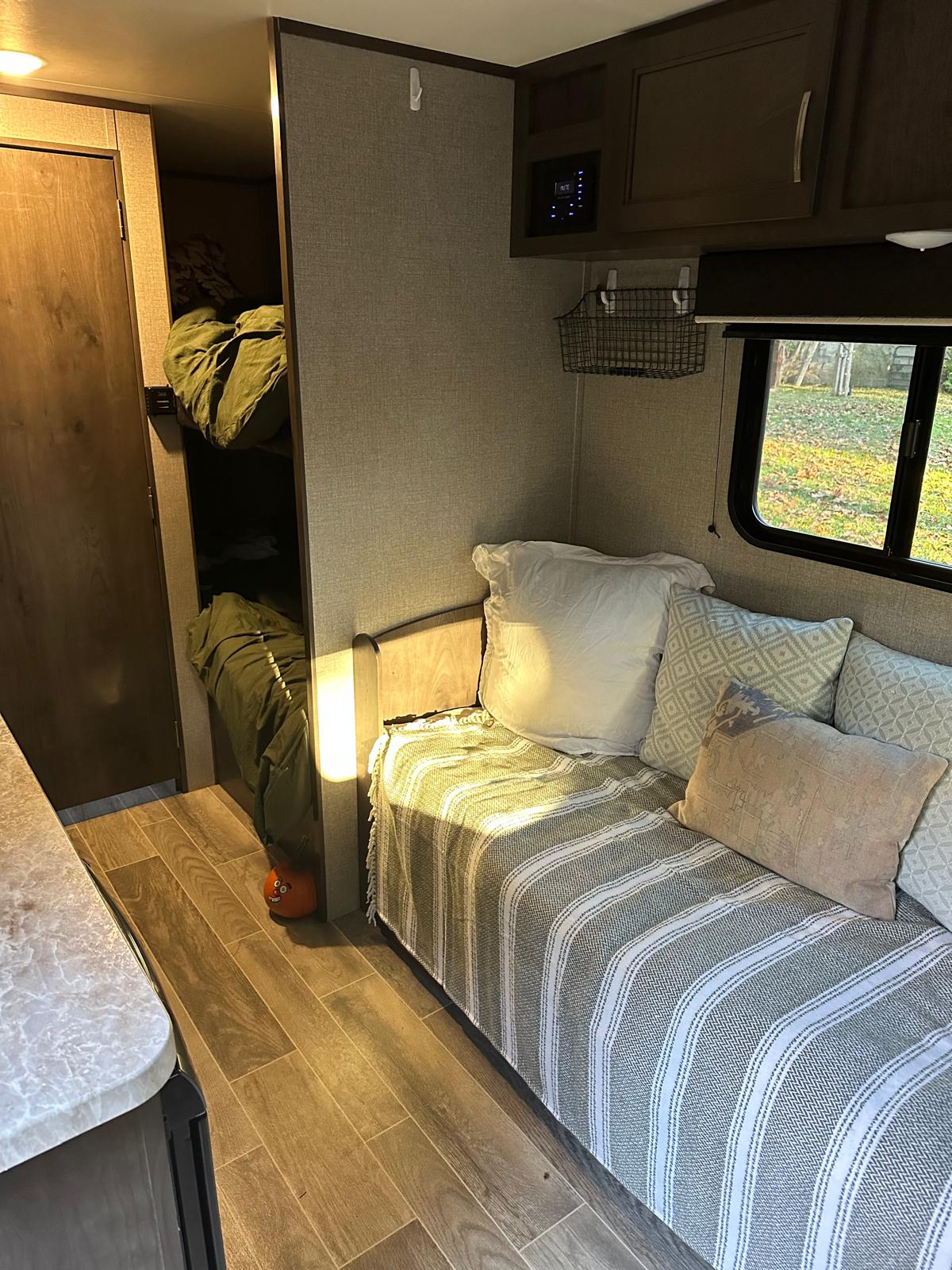 Explore this cozy RV rental interior featuring a striped daybed, comfy bunks with green bedding, and a window view.. Jayco Jay Flight 2021