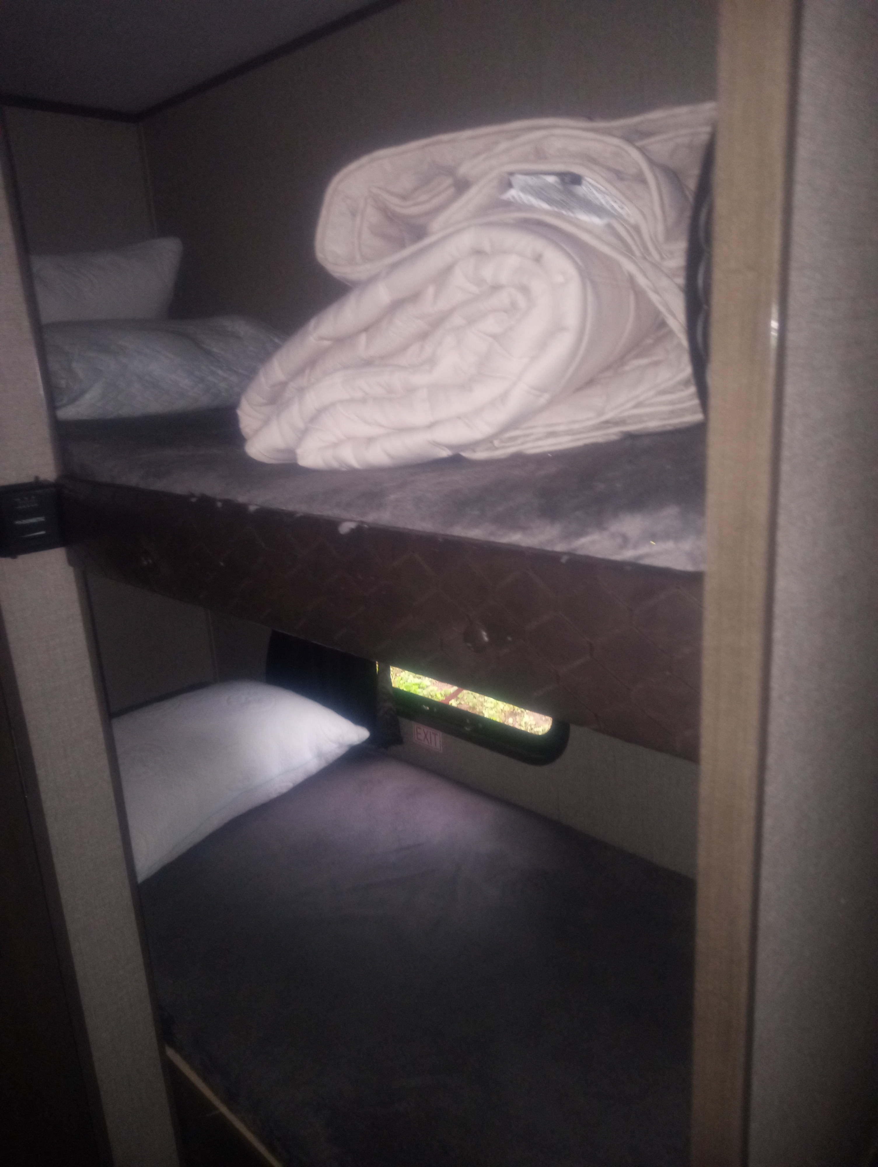 RV rental interior showing cozy bunk beds with pillows & blankets. Lower bunk features a small window with an exit sign & greenery.. Jayco Jay Flight 2021