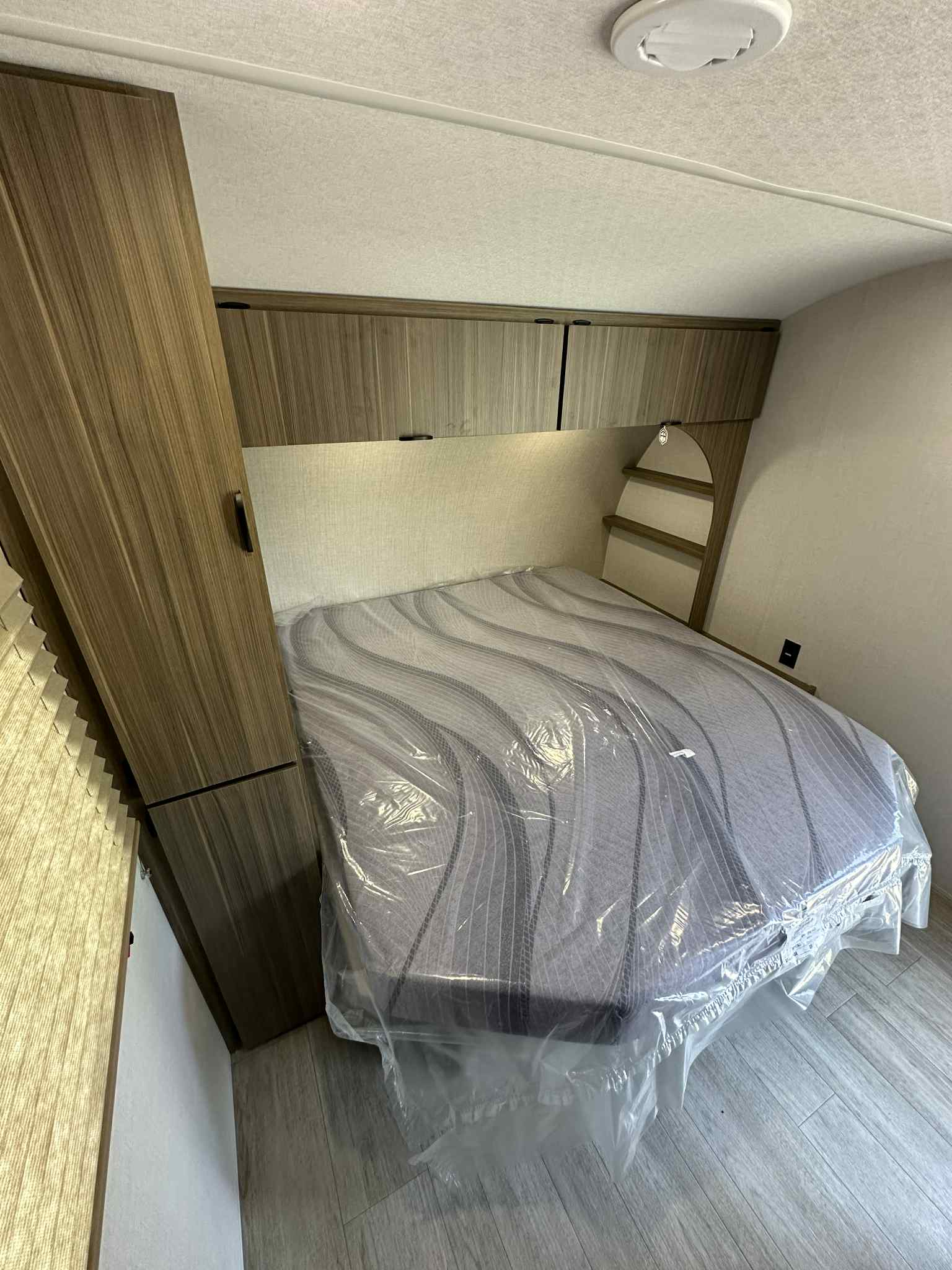 Modern RV rental bedroom featuring a protected mattress, ample wood-finish cabinetry, and a clean interior. Ideal for your travels.. Forest River Salem FSX 266BHLE 2026