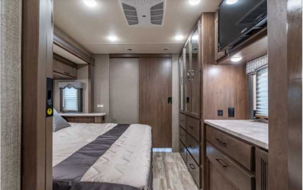 Well-appointed RV rental bedroom with a comfy bed, TV, window, and wood storage. Ideal for your next adventure.. Thor Hurricane 2021