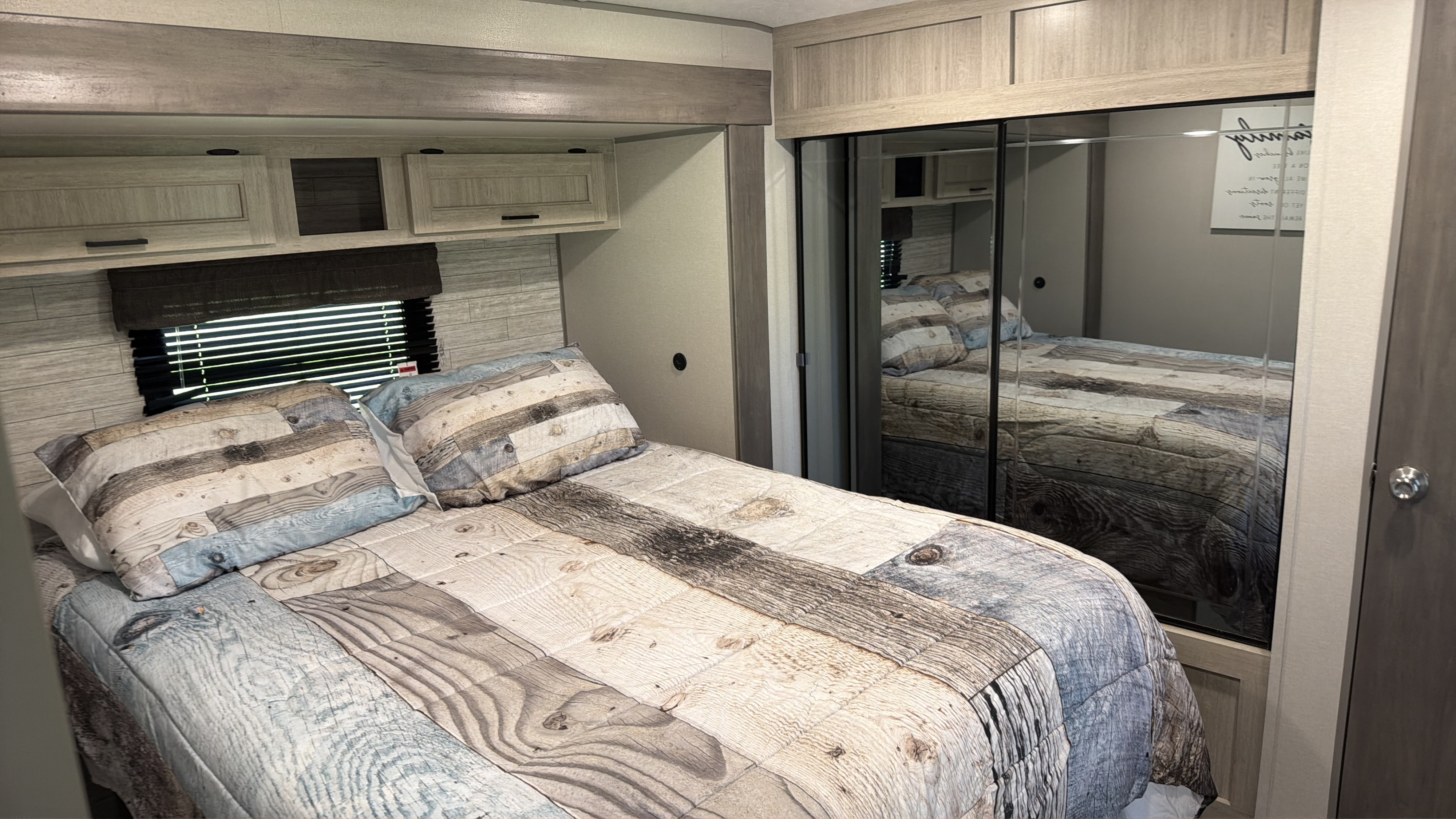 This RV rental bedroom features a comfy bed with unique wood-patterned bedding, overhead storage, and a mirrored closet.. Coachman Catalina, Legacy edition 343BHTS 2024