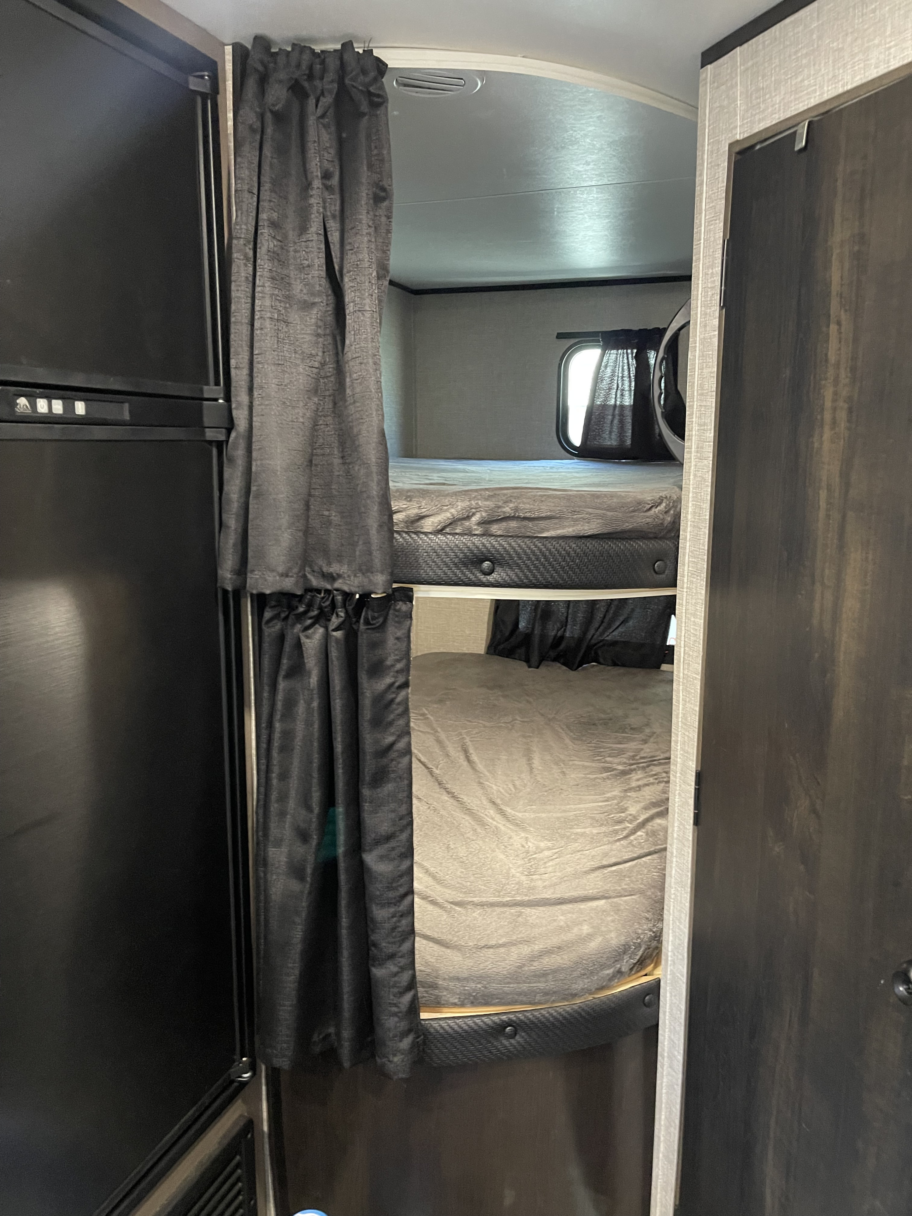 Inside an RV rental: dark-curtained bunk beds and a fridge, offering a cozy sleeping setup for travel.. Jayco Jay Flight SLX Rocky Mountain Edition 2021