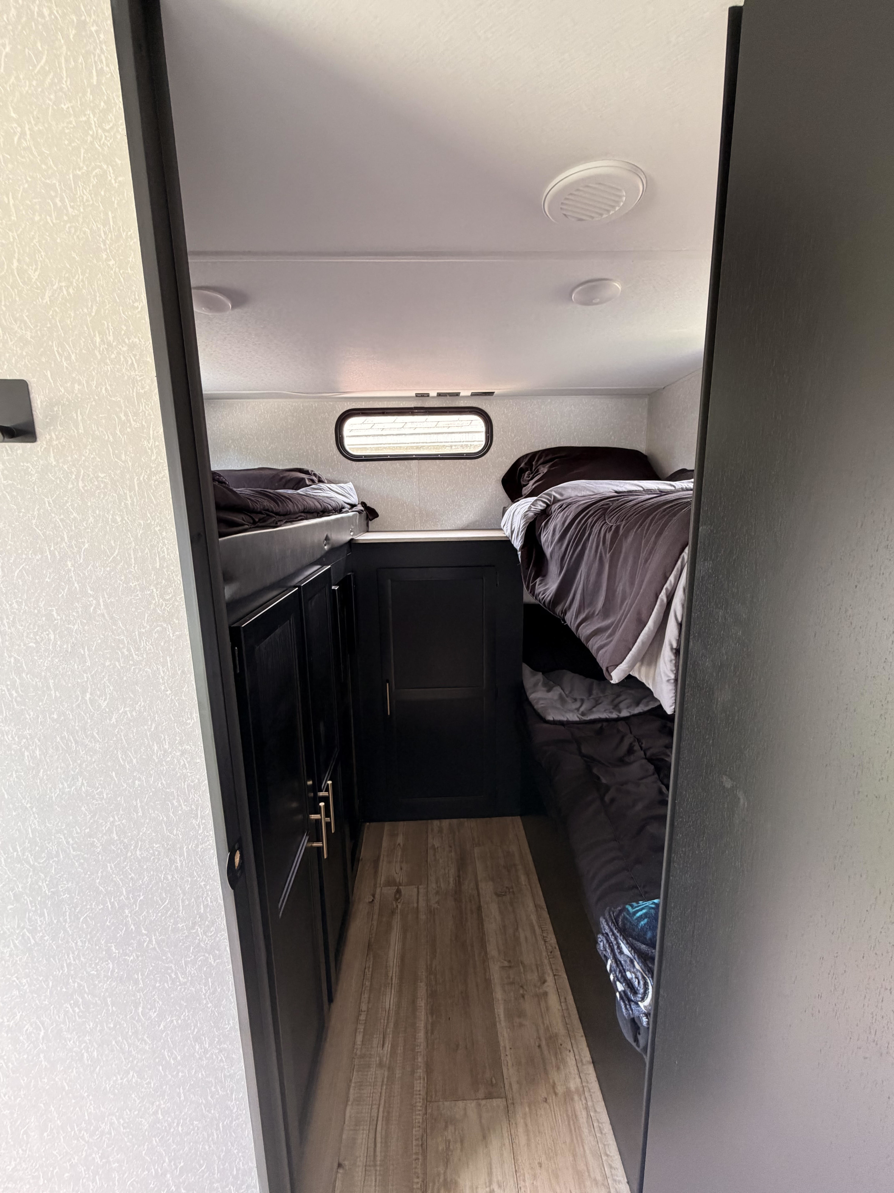 Cozy rv rental sleeping area: interior shot showing two bunk beds with dark bedding, black cabinets, and wood-look floor.. Forest River Cherokee Grey Wolf 2022