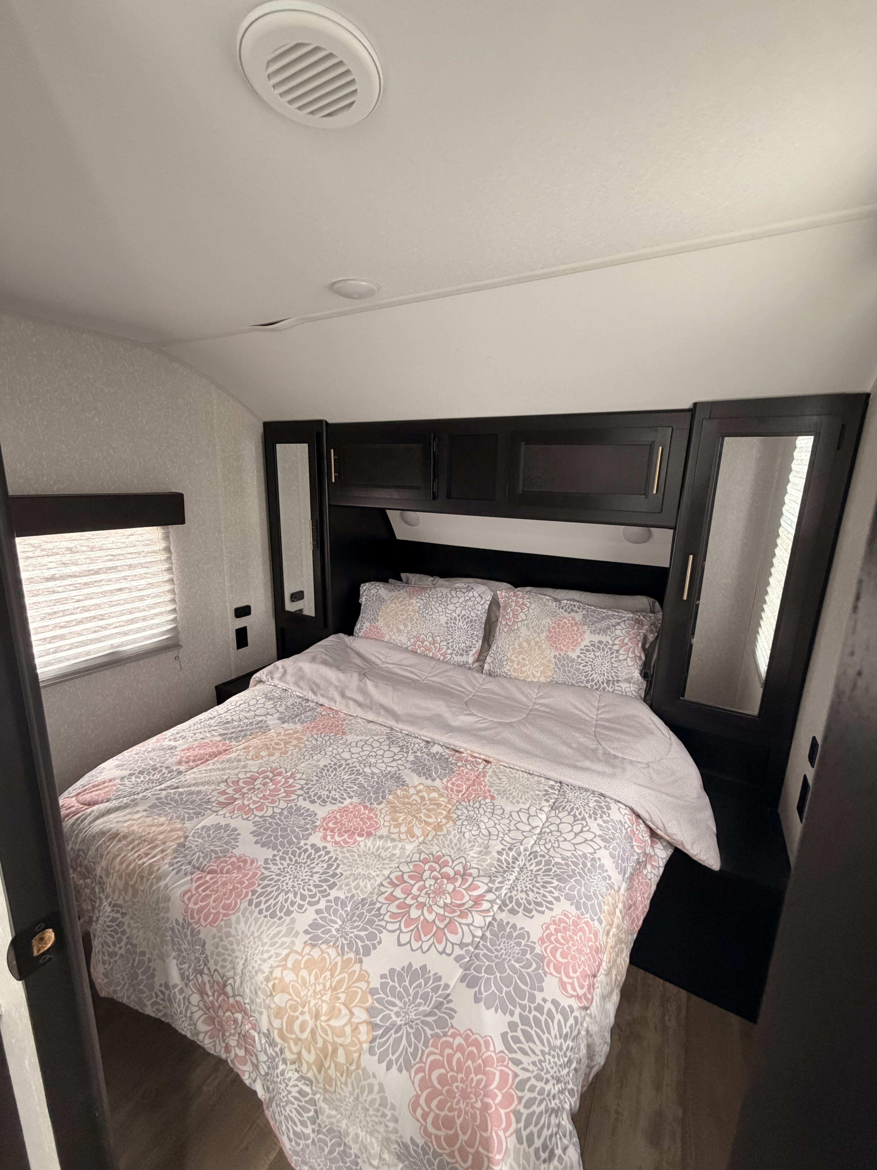 Bright rv rental bedroom with floral bedding, overhead cabinets, and mirrored wardrobes for a cozy stay.. Forest River Cherokee Grey Wolf 2022