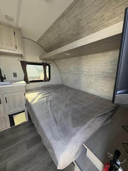 RV rental interior featuring a compact bedroom with a gray patterned bed, wood-look walls, cabinet storage, and a small window.. 5ZT2CABC9TK012992 Catalina 2026