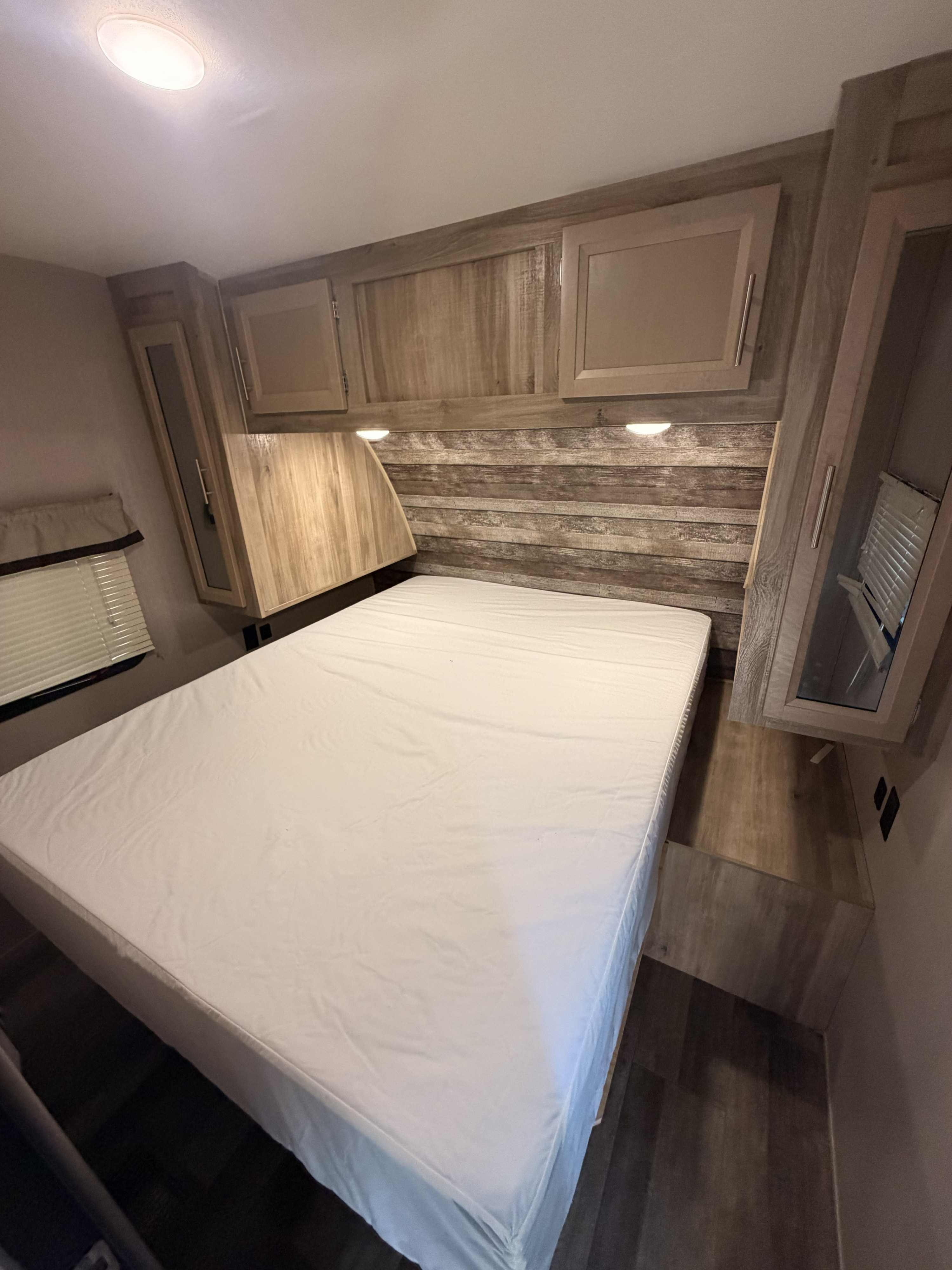 Cozy RV rental bedroom features a comfortable bed, wood paneling, overhead cabinets, and a window with blinds.. Coachmen Other 2021