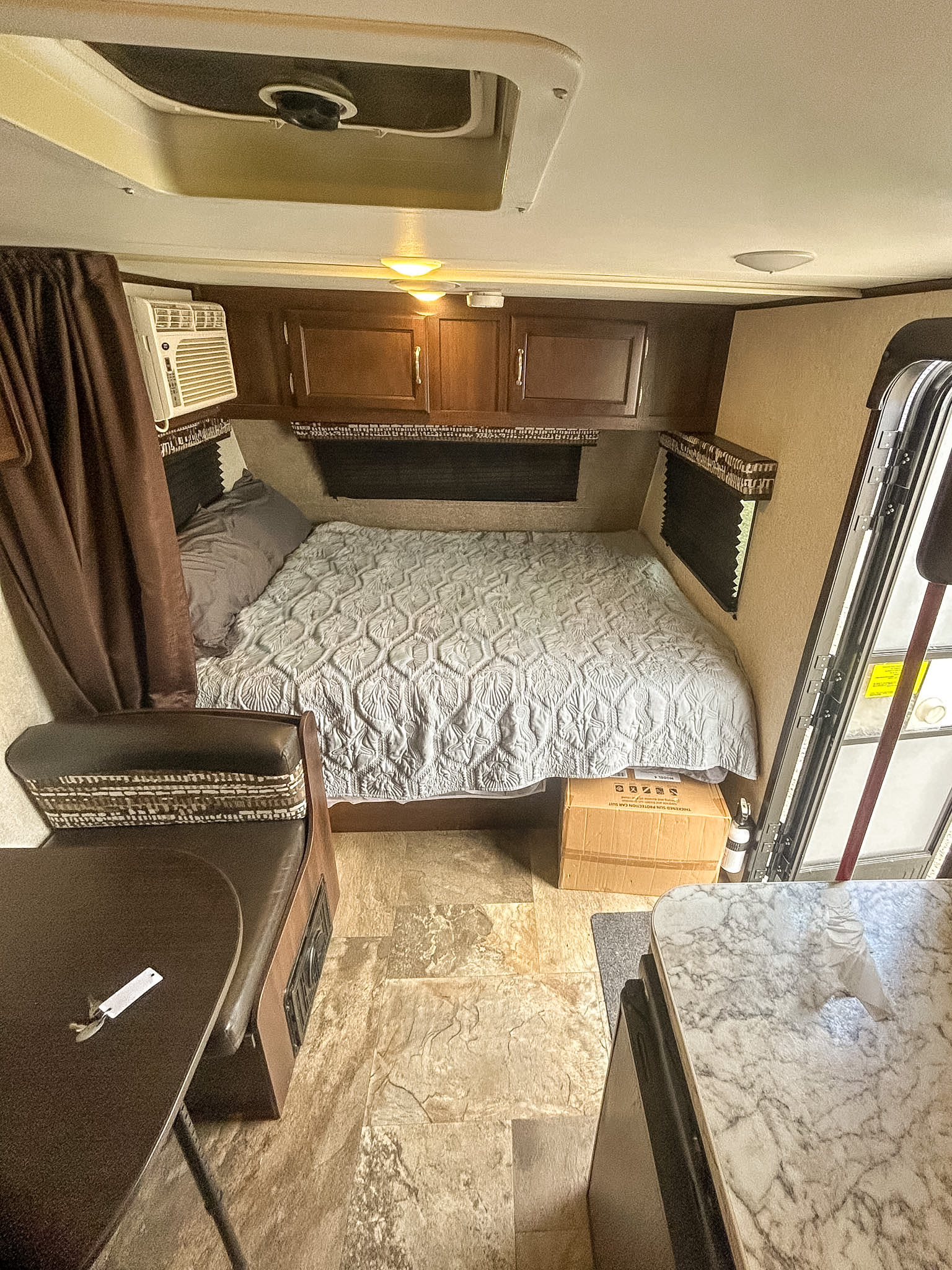 Inside an rv rental: a compact living space showing a bed with quilt, AC unit, wood cabinets, a dinette, and kitchen counter.. Jayco Jay Flight SLX 2018