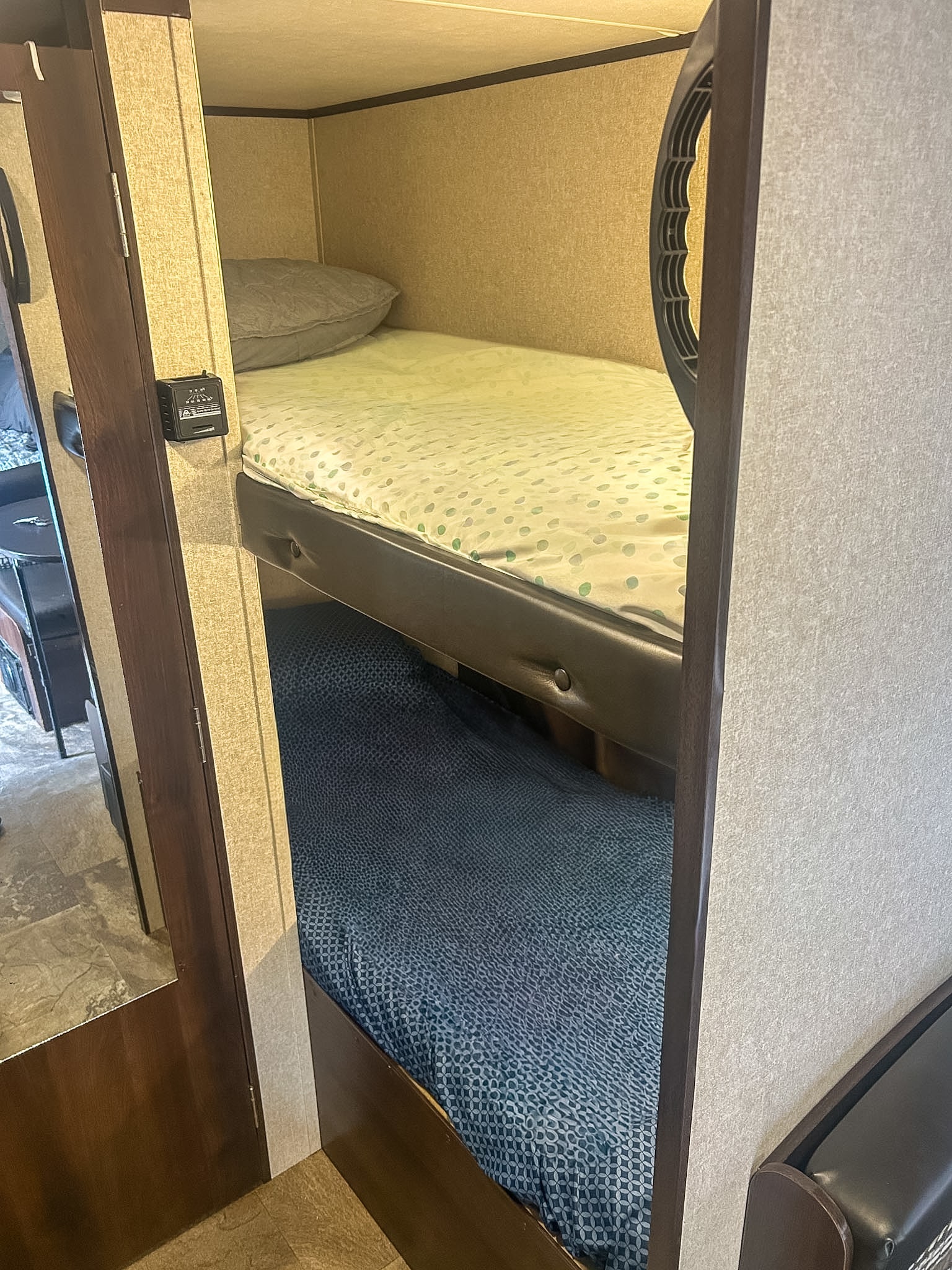 Inside an RV rental: close-up of compact bunk beds with polka-dot and blue patterned sheets, a control panel on the wall.. Jayco Jay Flight SLX 2018