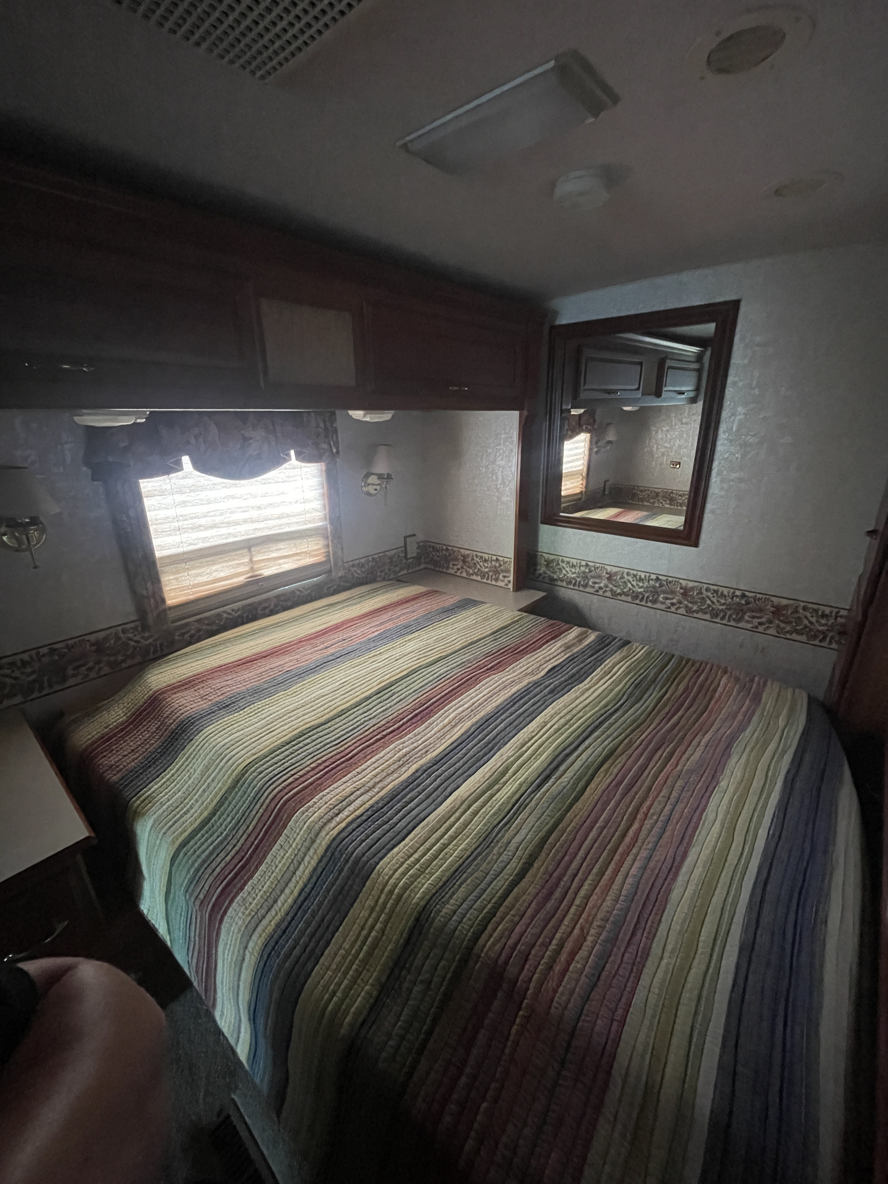 RV rental bedroom featuring a colorful striped bed, overhead cabinets, and a framed mirror. Ideal for your next trip.. Winnebago Chieftain 1999