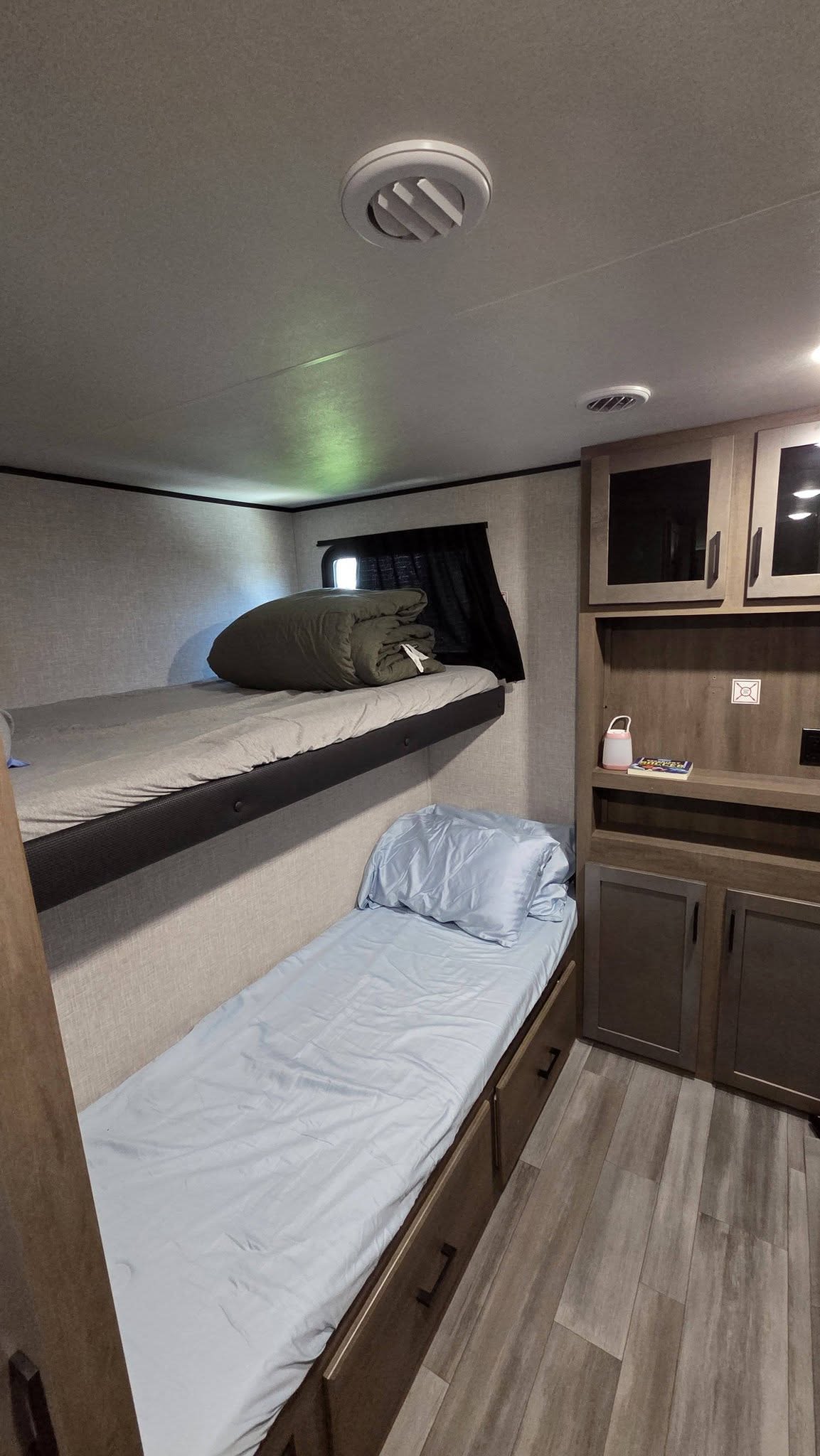 Inside an RV rental: a cozy bunk bed sleeping area with light blue bedding, storage cabinets, and wood-look flooring.. Jayco Jay Flight 2024