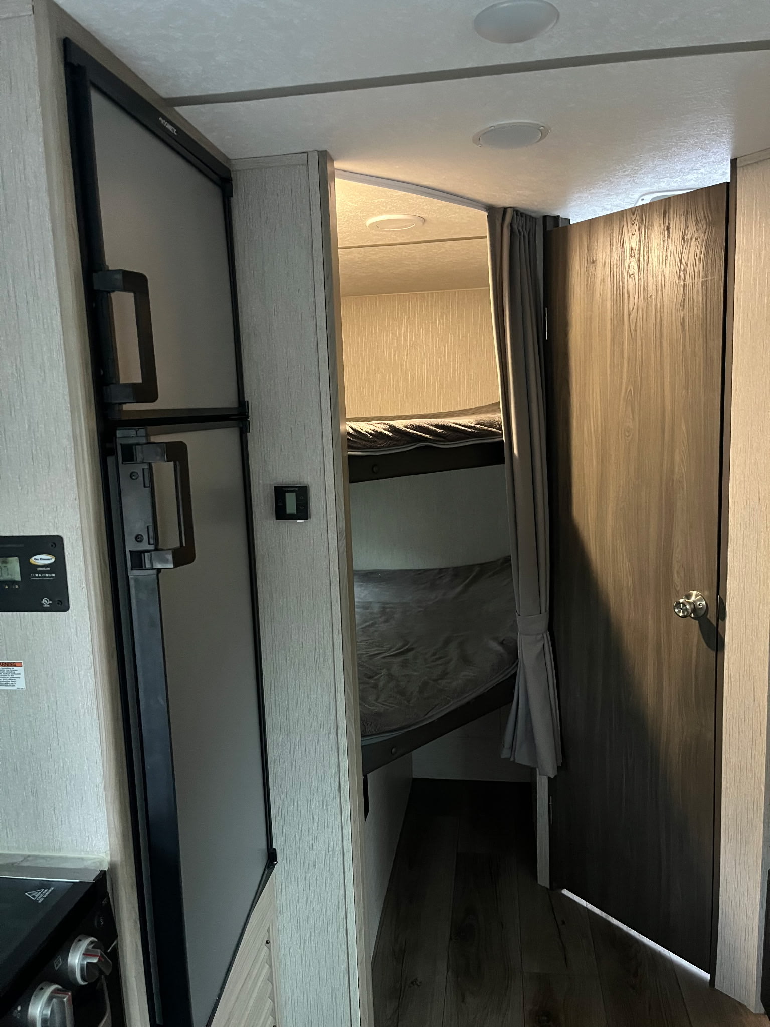 This cozy rv rental interior features a Dometic refrigerator, bunk beds with gray privacy curtain, and a dark wood door.. Coachmen freedom express 2021
