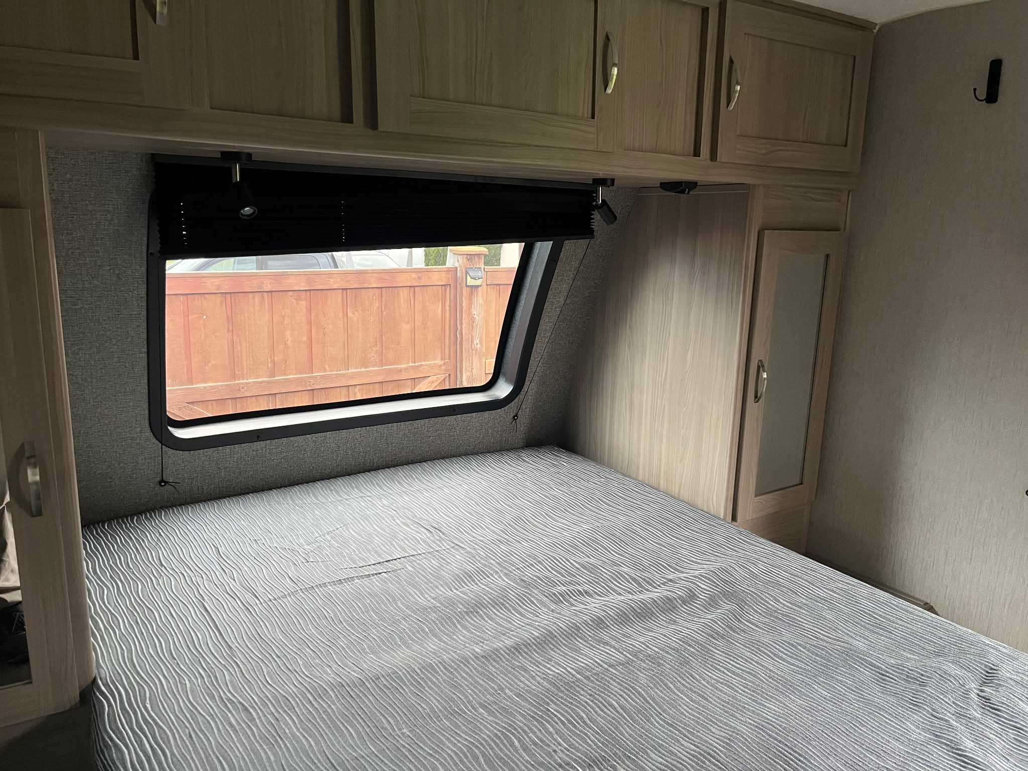 Cozy RV rental bedroom featuring a patterned bedspread, overhead storage, a window with blinds, and a small mirrored closet.. Coachmen freedom express 2021