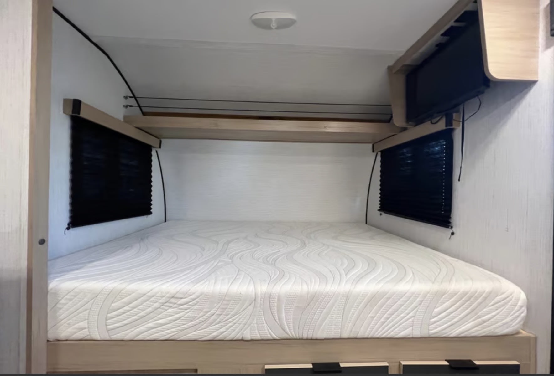 Clean RV rental bedroom featuring a comfy mattress, black window blinds, overhead shelf, and a wall-mounted TV.. Cruiser RV Hitch 2022