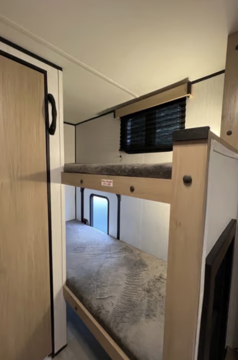 Inside an rv rental: sturdy bunk beds with grey mattresses, a top window, and a bright lower window for light.. Cruiser RV Hitch 2022