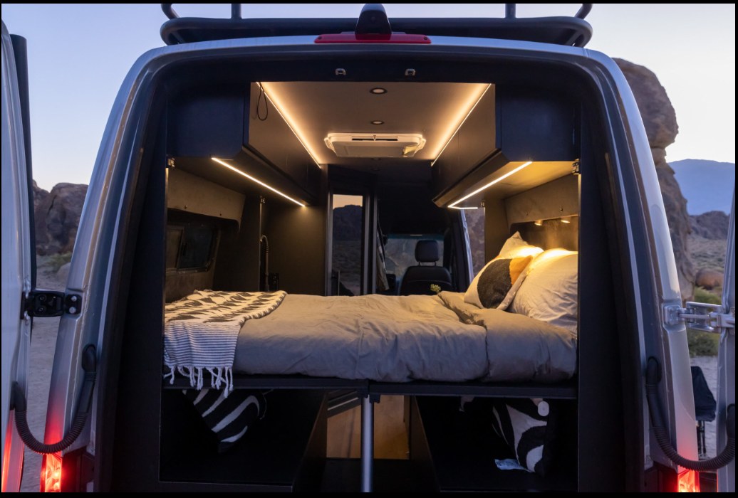 Inside this RV rental: a modern camper van interior with a cozy bed, bright LED lighting, and practical storage.. Mercedes Sprinter 144 2020