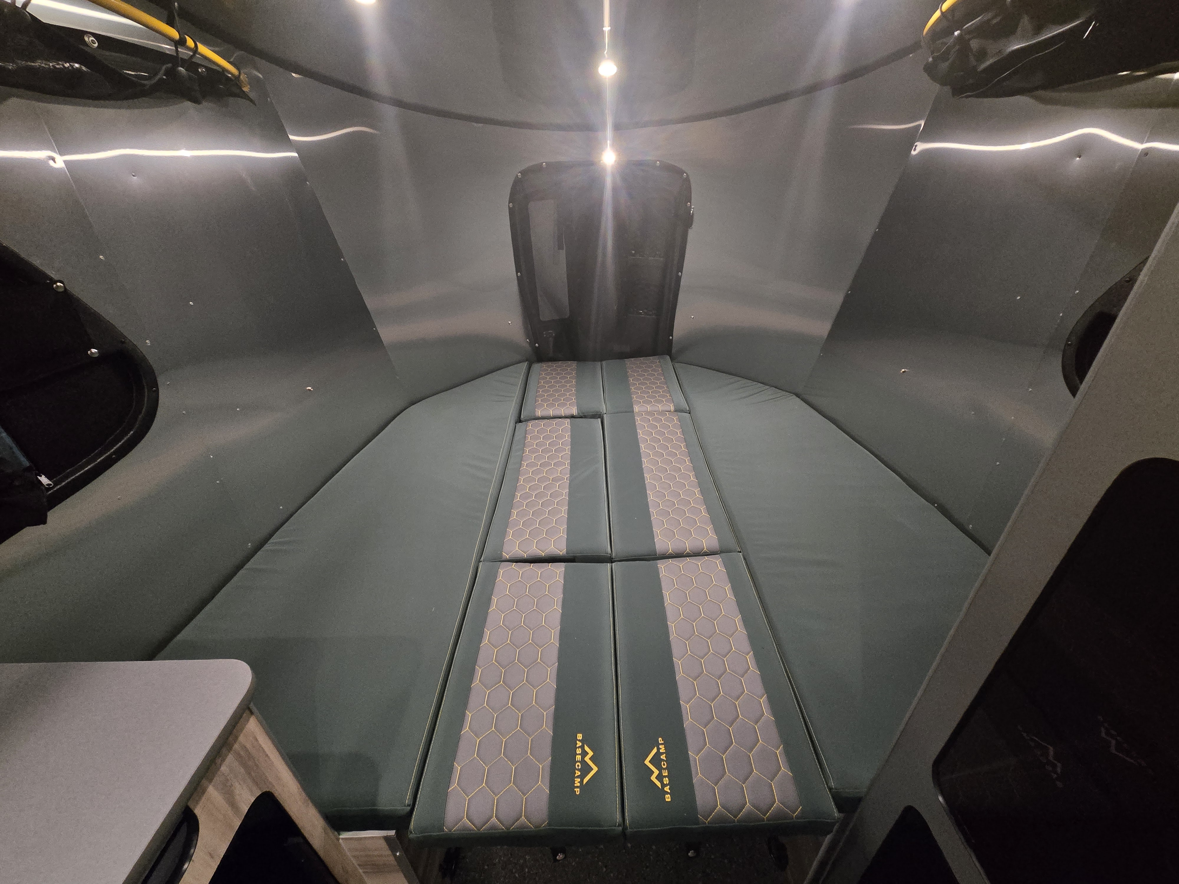 Cozy rv rental interior with green mattresses, metallic walls, and a small table. Perfect for camping adventures.. Airstream Basecamp 2022