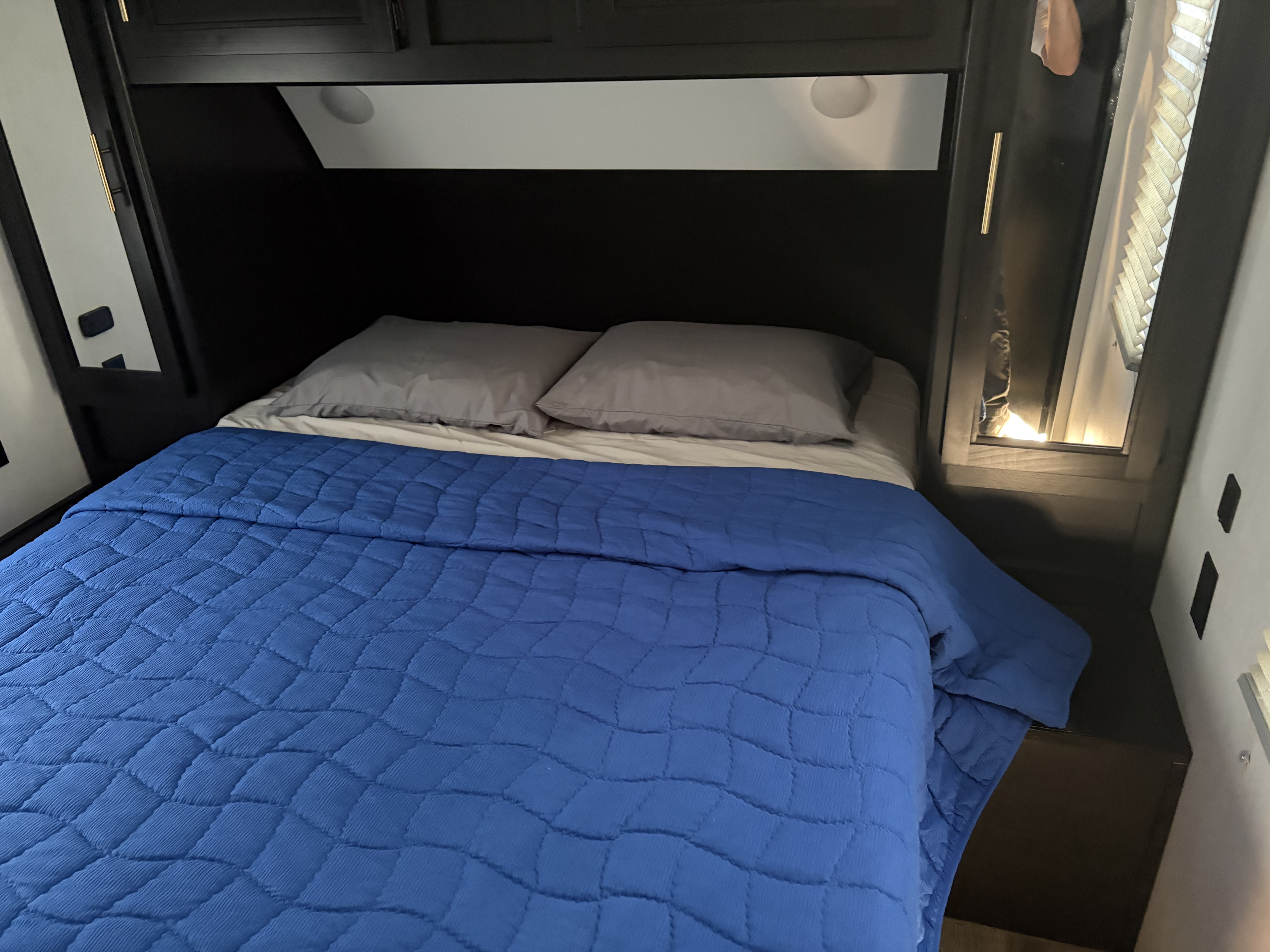 Compact RV rental bedroom with a comfy bed, blue quilted comforter, gray pillows, and built-in storage. Perfect for travel.. Forest River Cherokee 2023
