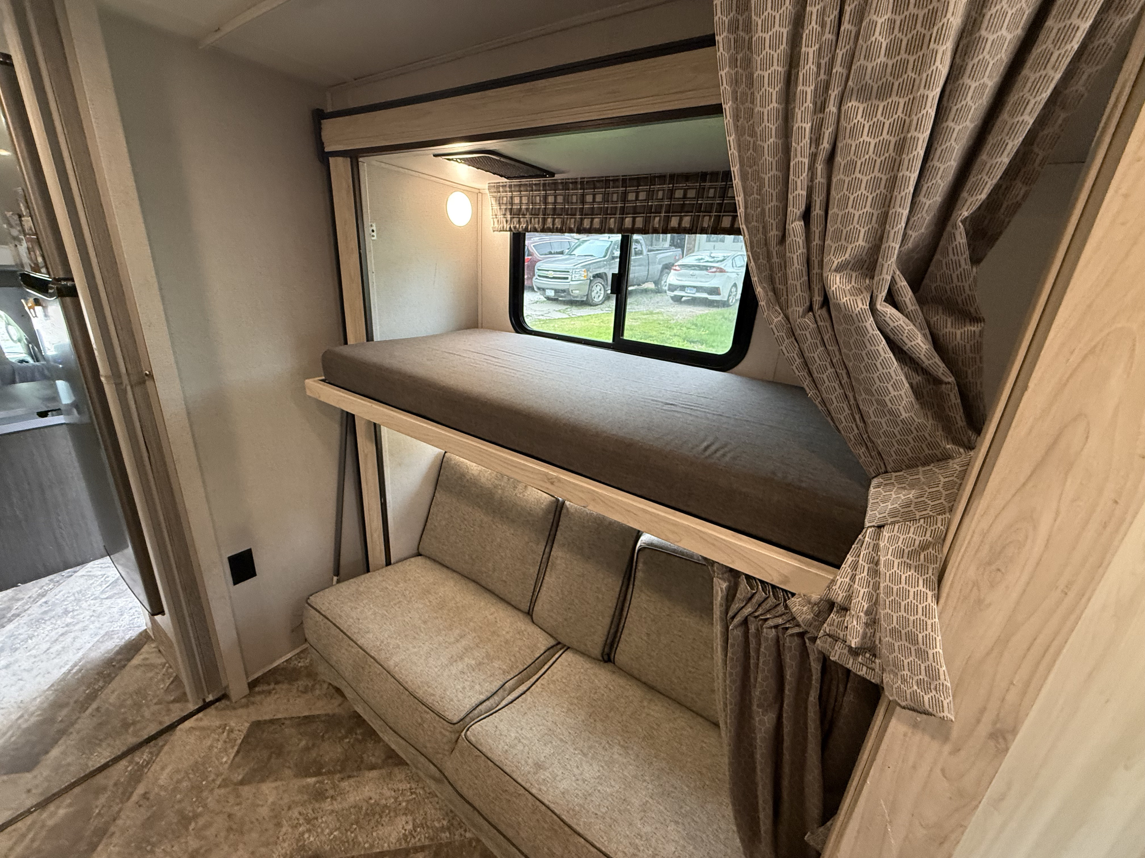 RV rental interior: bunk bed with gray mattress over a comfortable light-colored sofa, geometric curtains, and a window.. Forest River Sunseeker LE 2021