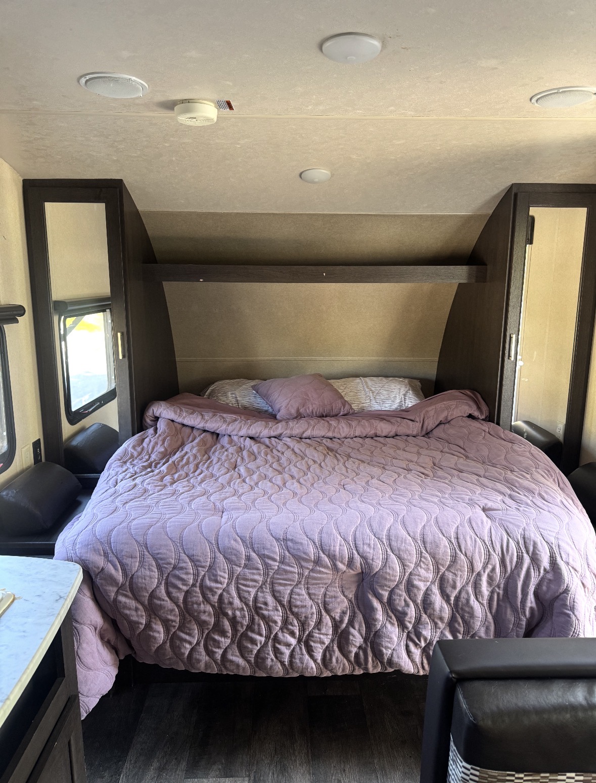 RV rental bedroom: A comfortable bed with a purple quilted comforter and dark wood storage in a cozy RV interior.. Forest River Wildwood X-Lite 2019