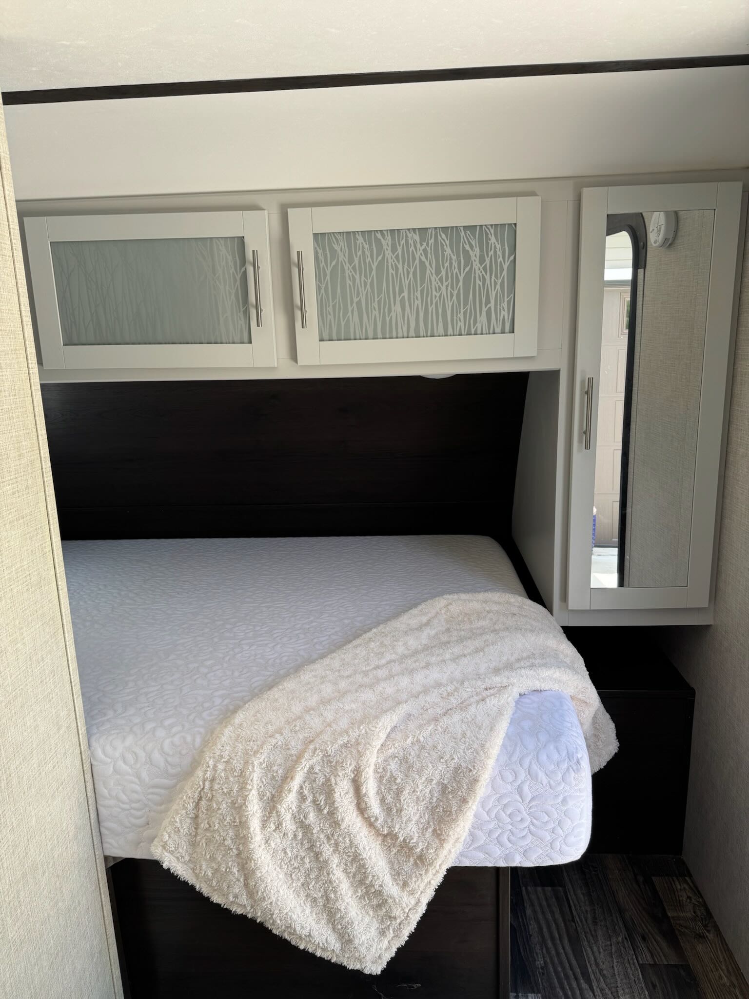 Comfortable RV rental bedroom with a white quilted bed, dark headboard, patterned overhead cabinets, and mirrored storage.. Keystone RV Bullet Crossfire 2019