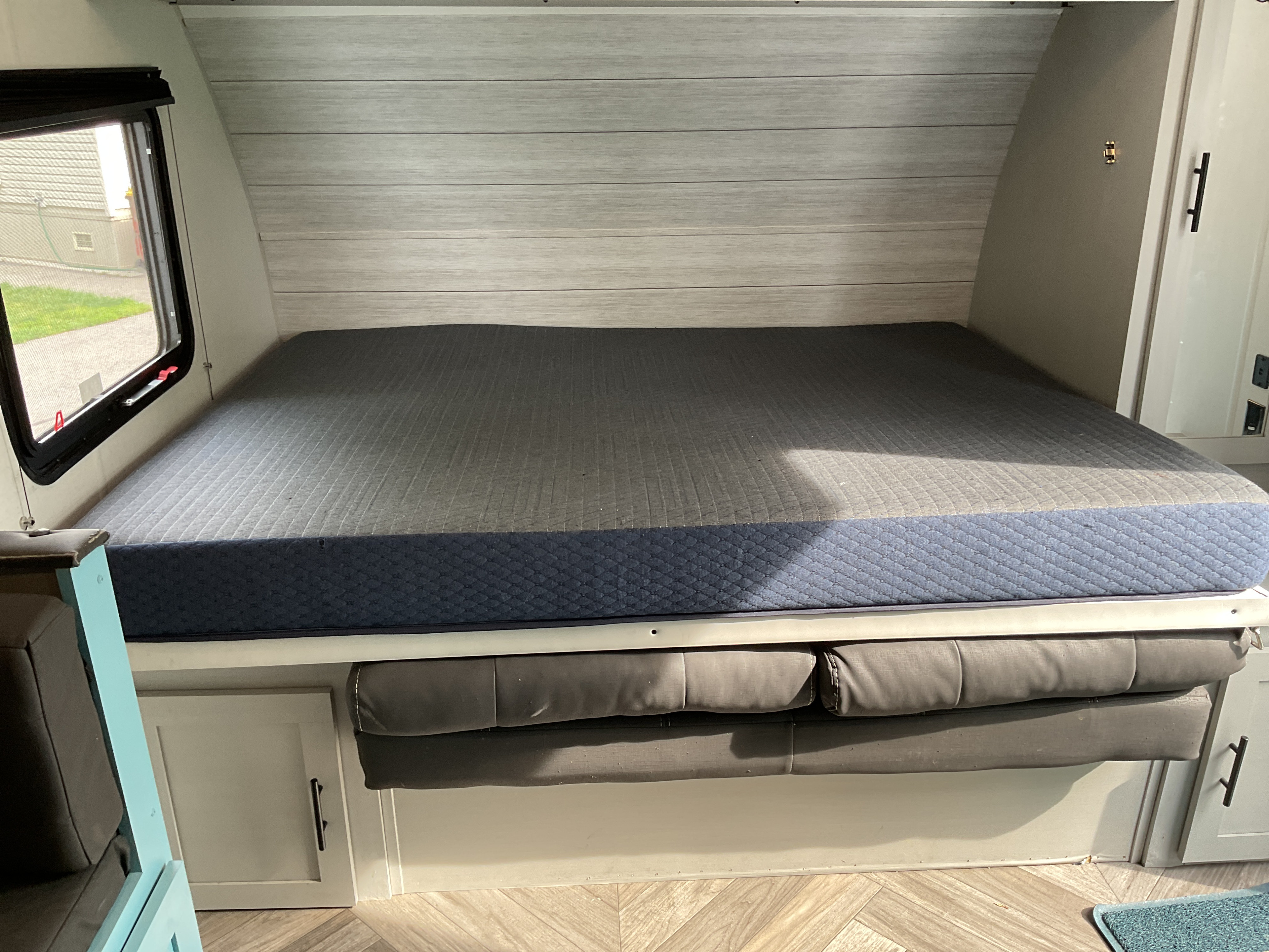 Inside an RV rental: a spacious bed with blue and grey quilted mattress, flanked by a window and storage, likely convertible dinette.. Forest River Salem 2021