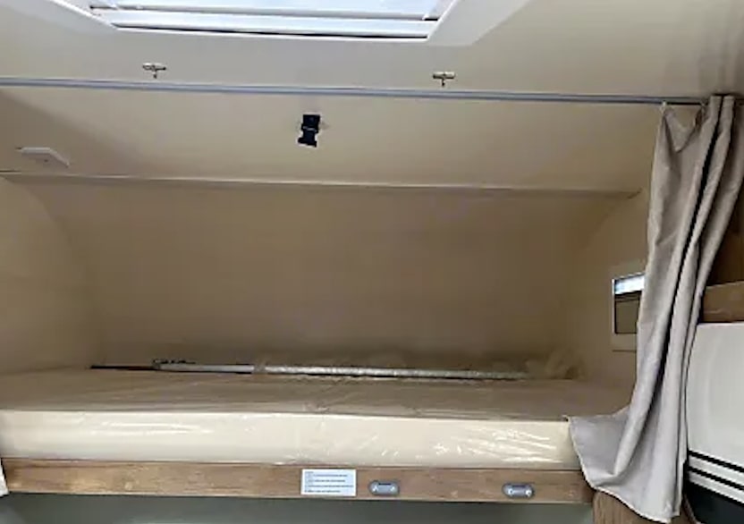 Inside an RV rental: a bunk bed with a clean mattress, small window, and light curtain.. CI HORON 2023