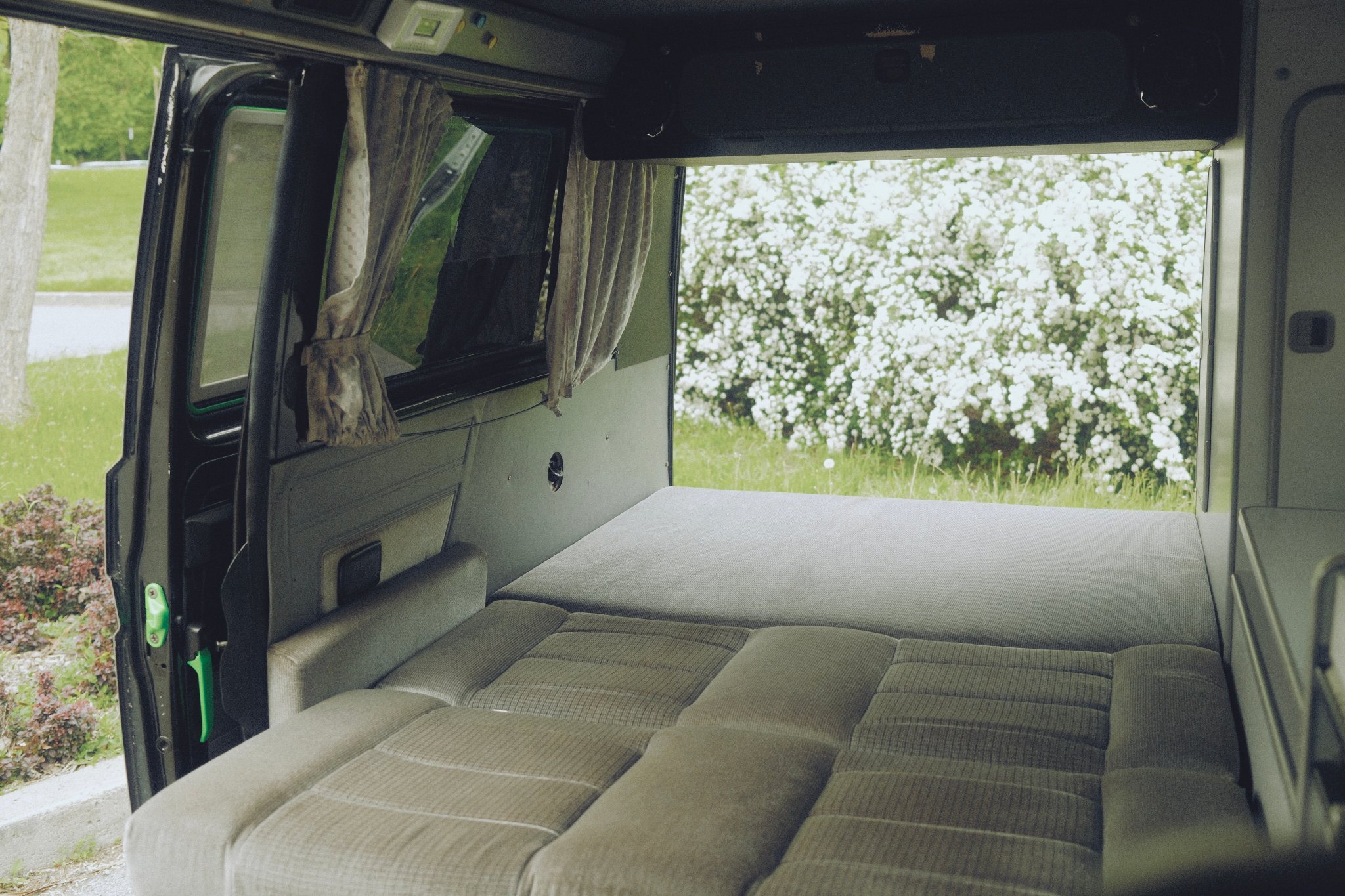 Cozy RV rental interior with a convertible bed/couch, offering a serene view of a flowering bush outside.. Volkswagen Westfalia 1988