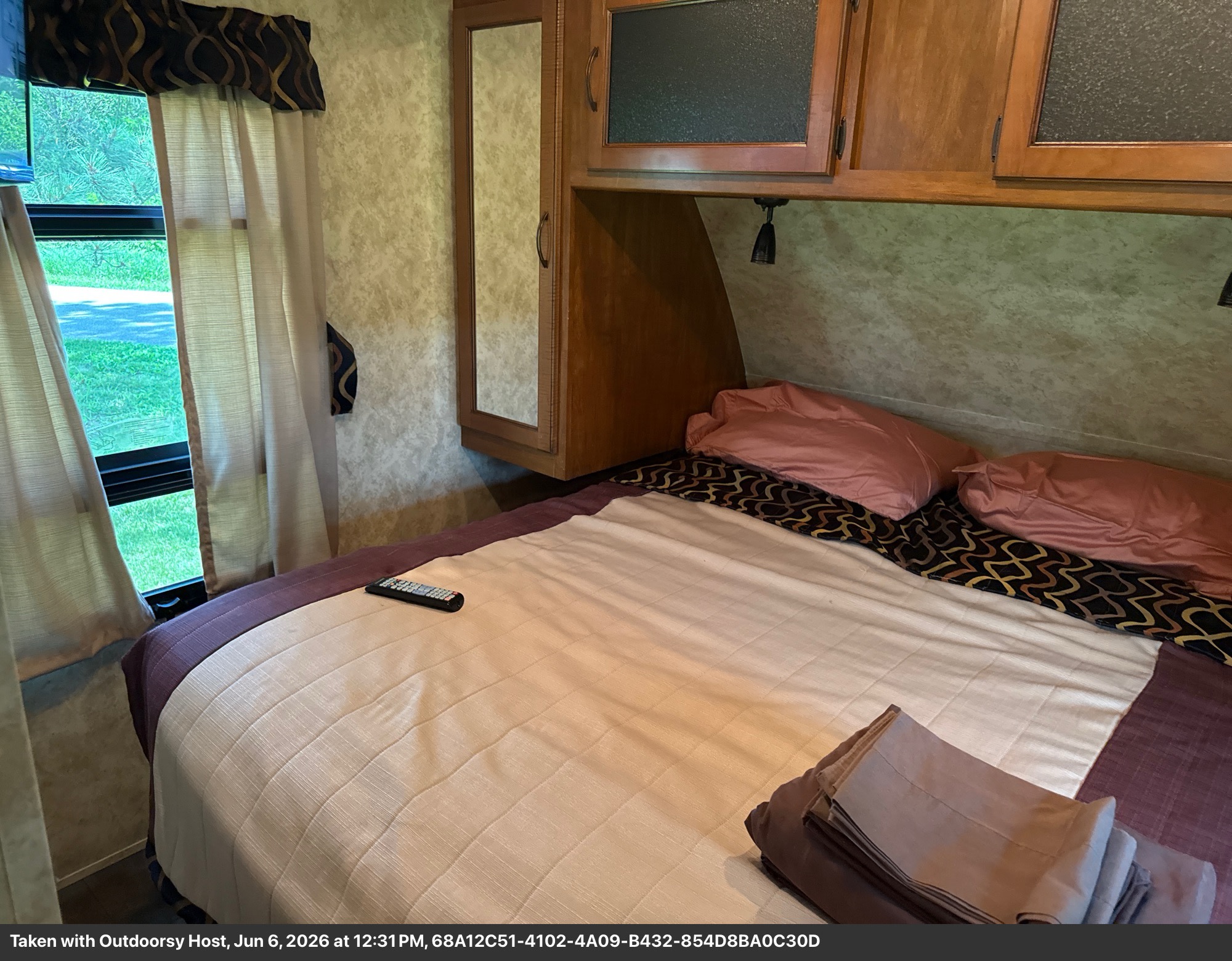 Comfortable RV rental bedroom with a queen bed, overhead storage, and a window offering a scenic outdoor view.. Keystone RV Bullet Ultra Lite 2011