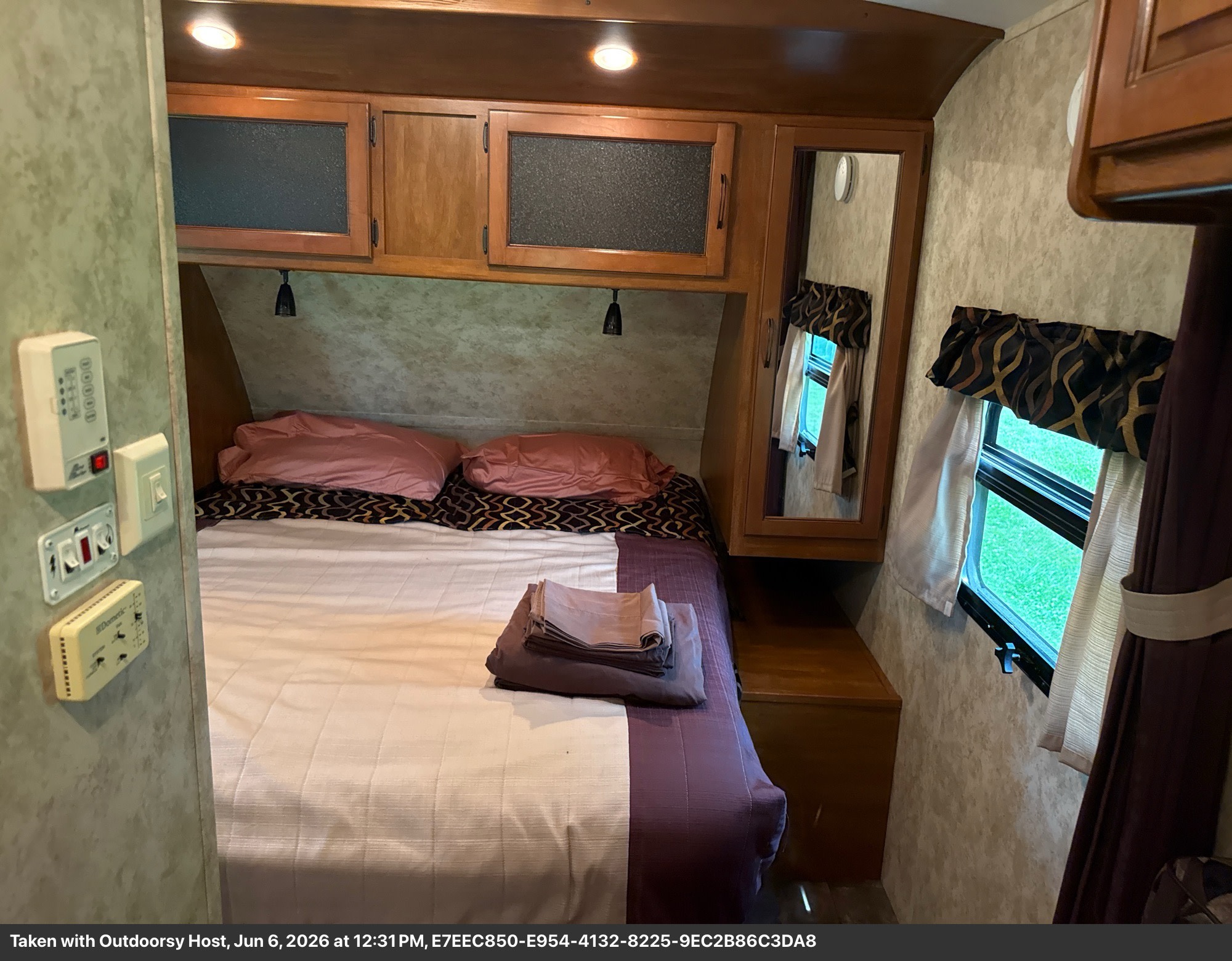 Cozy RV rental bedroom featuring a comfortable bed with pillows, overhead cabinets, a window, and a wall-mounted thermostat.. Keystone RV Bullet Ultra Lite 2011