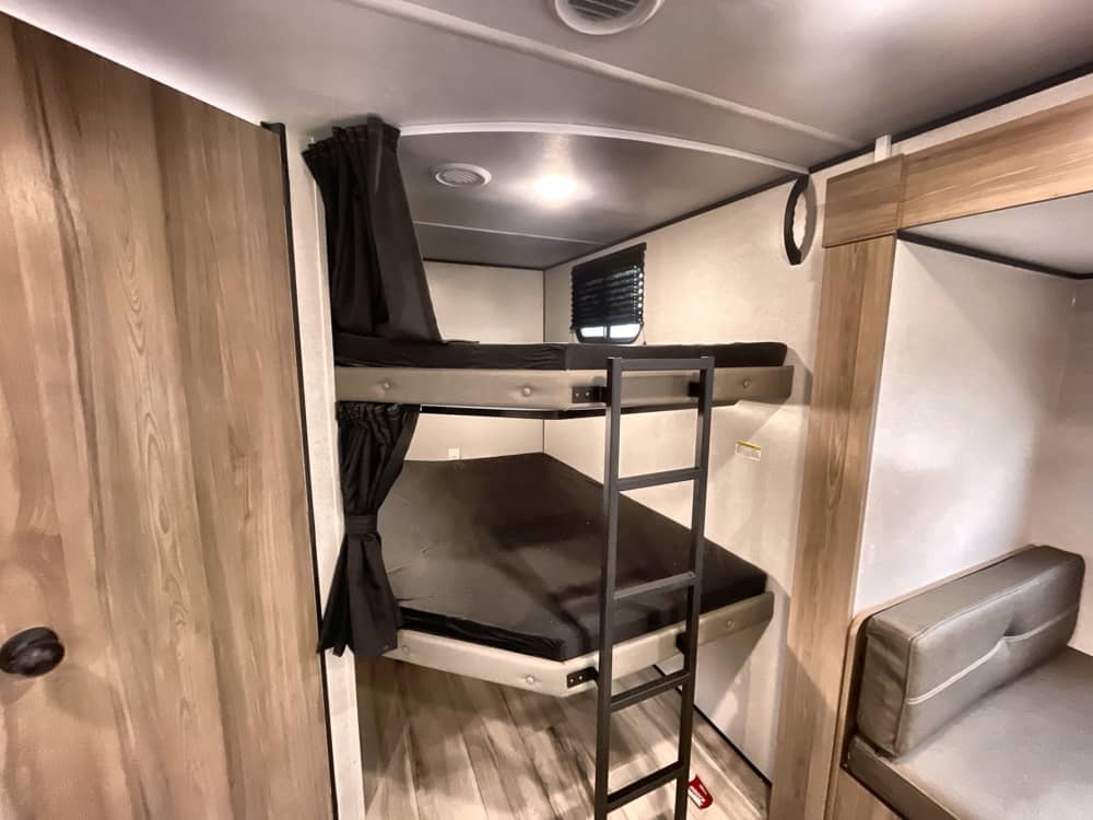 This RV rental features stacked bunk beds with privacy curtains and a ladder, offering compact sleeping for travelers.. Keystone RV COLEMAN LITE 2026
