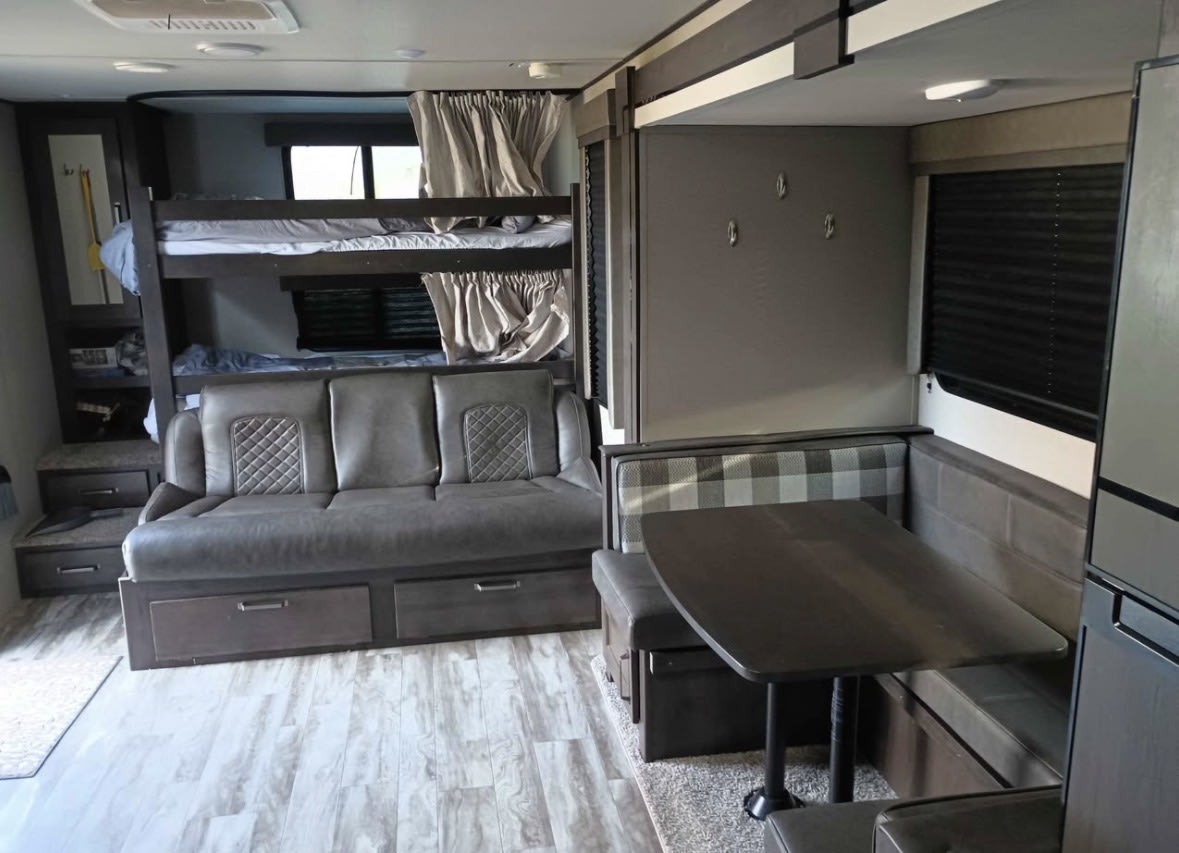 Explore this comfortable RV rental interior, featuring practical bunk beds, a sofa with storage, and a dinette for your camper adventures.. Grand Design Transcend Xplor 2022