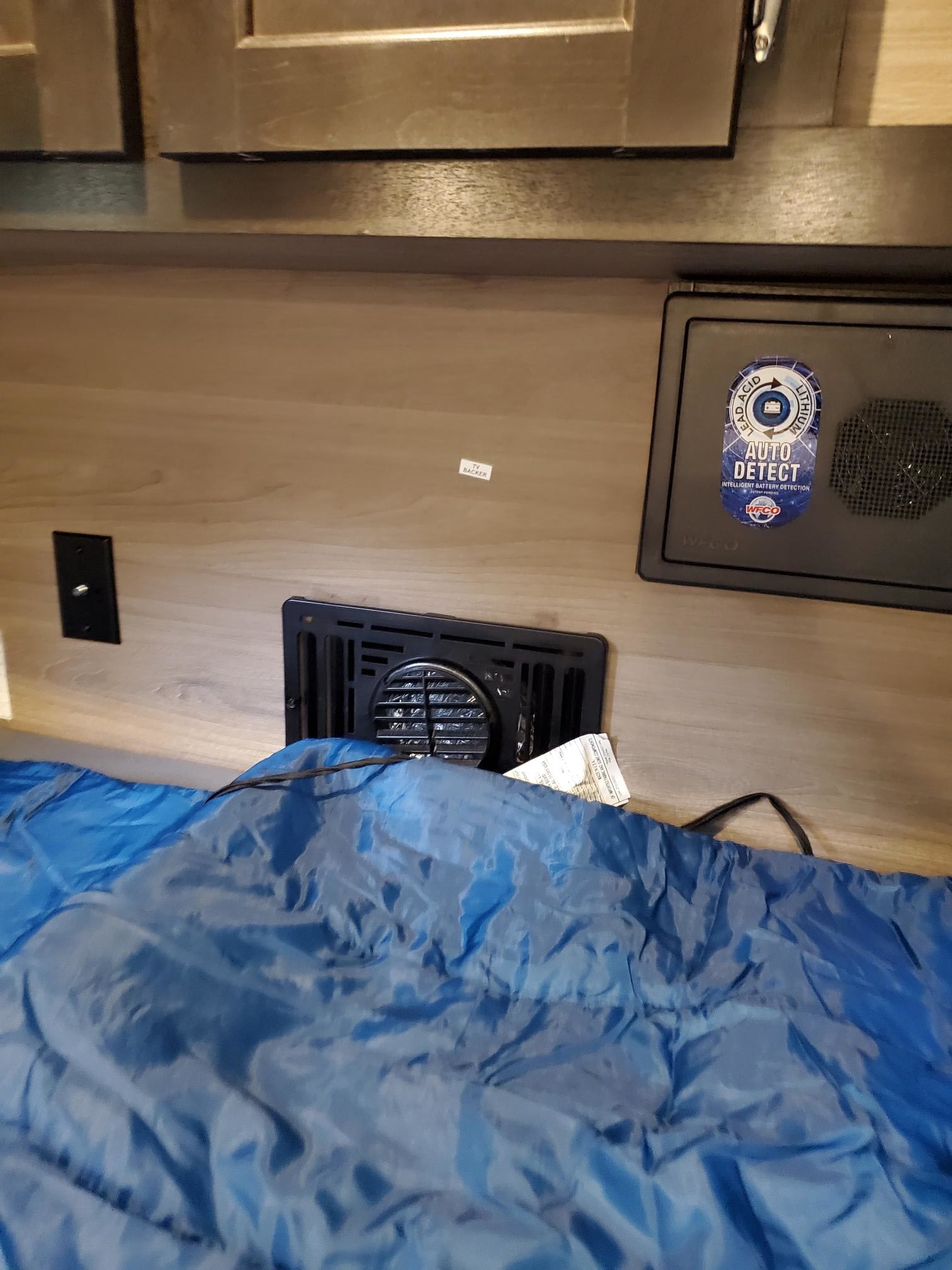 RV rental interior: WFCO battery detection panel, vent, and outlet, with a blue sleeping bag partly covering the vent.. Braxton Creek Bushwhacker 2024