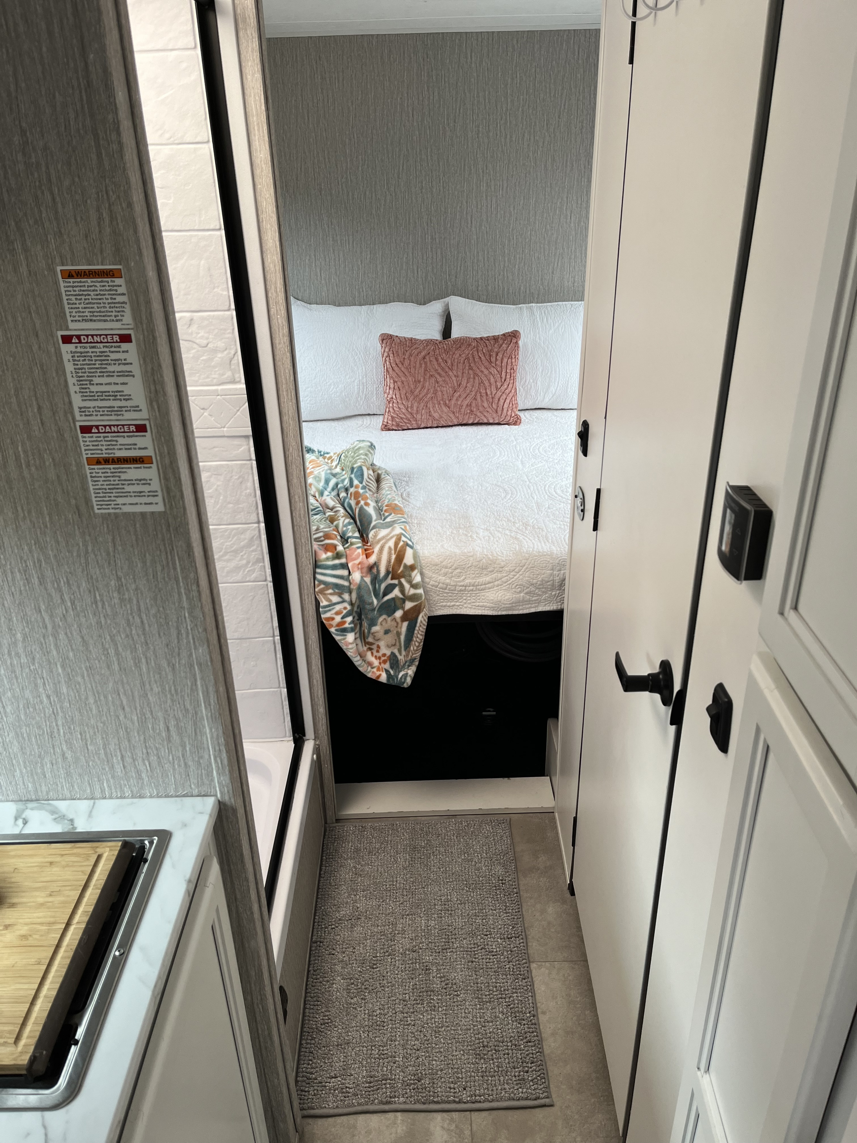 RV rental interior: A compact bedroom with a bed and blanket is seen past a kitchen counter with safety warnings on the wall.. Coachmen Cross Trail 2022