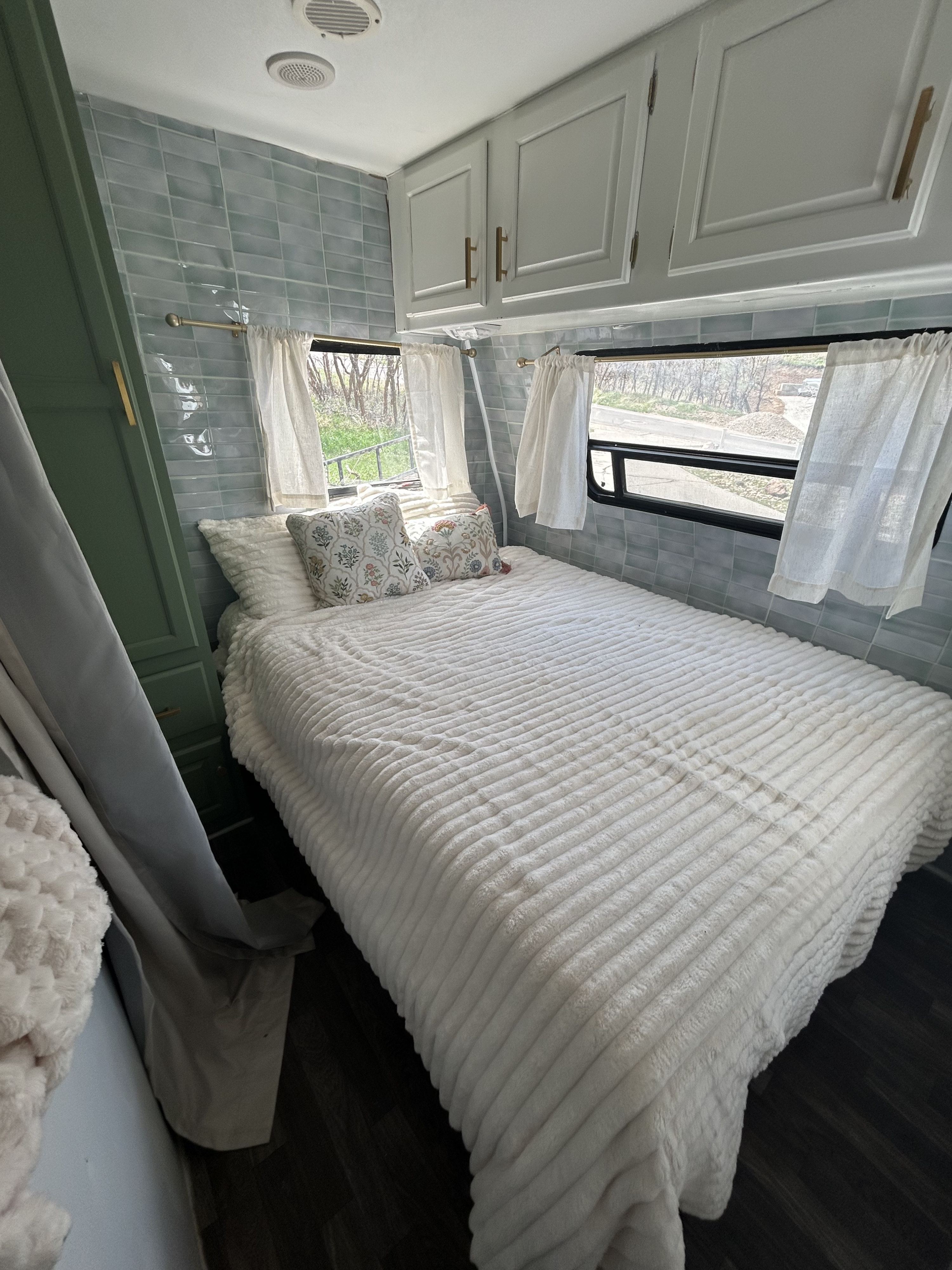 Inside this cozy rv rental, a bedroom with a plush bed, light blue tiled walls, and bright windows offering outdoor views.. Fleetwood Prowler 1997