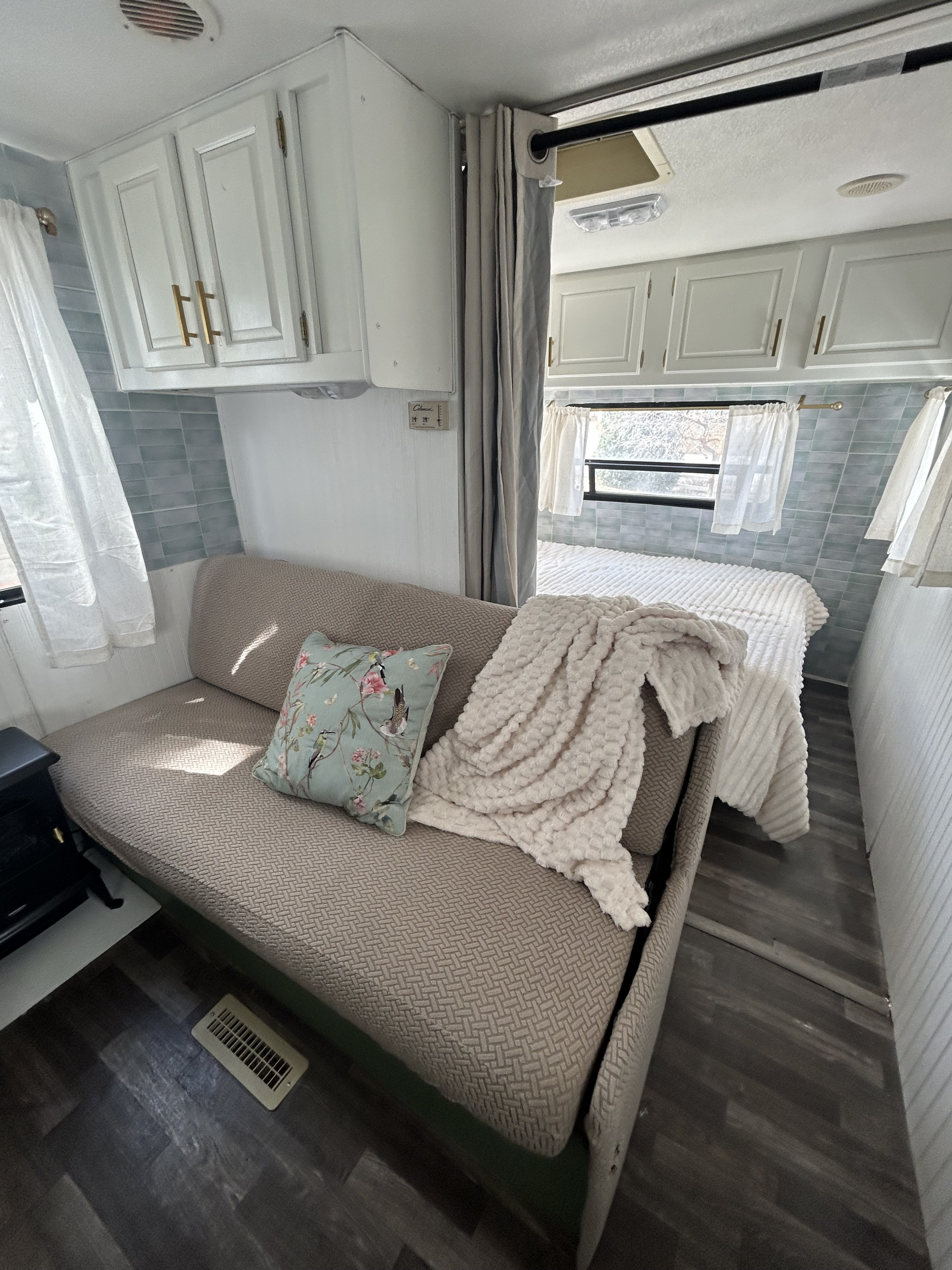 Cozy rv rental interior, featuring a bright living area with a textured couch, decorative pillow, and a partitioned bed.. Fleetwood Prowler 1997