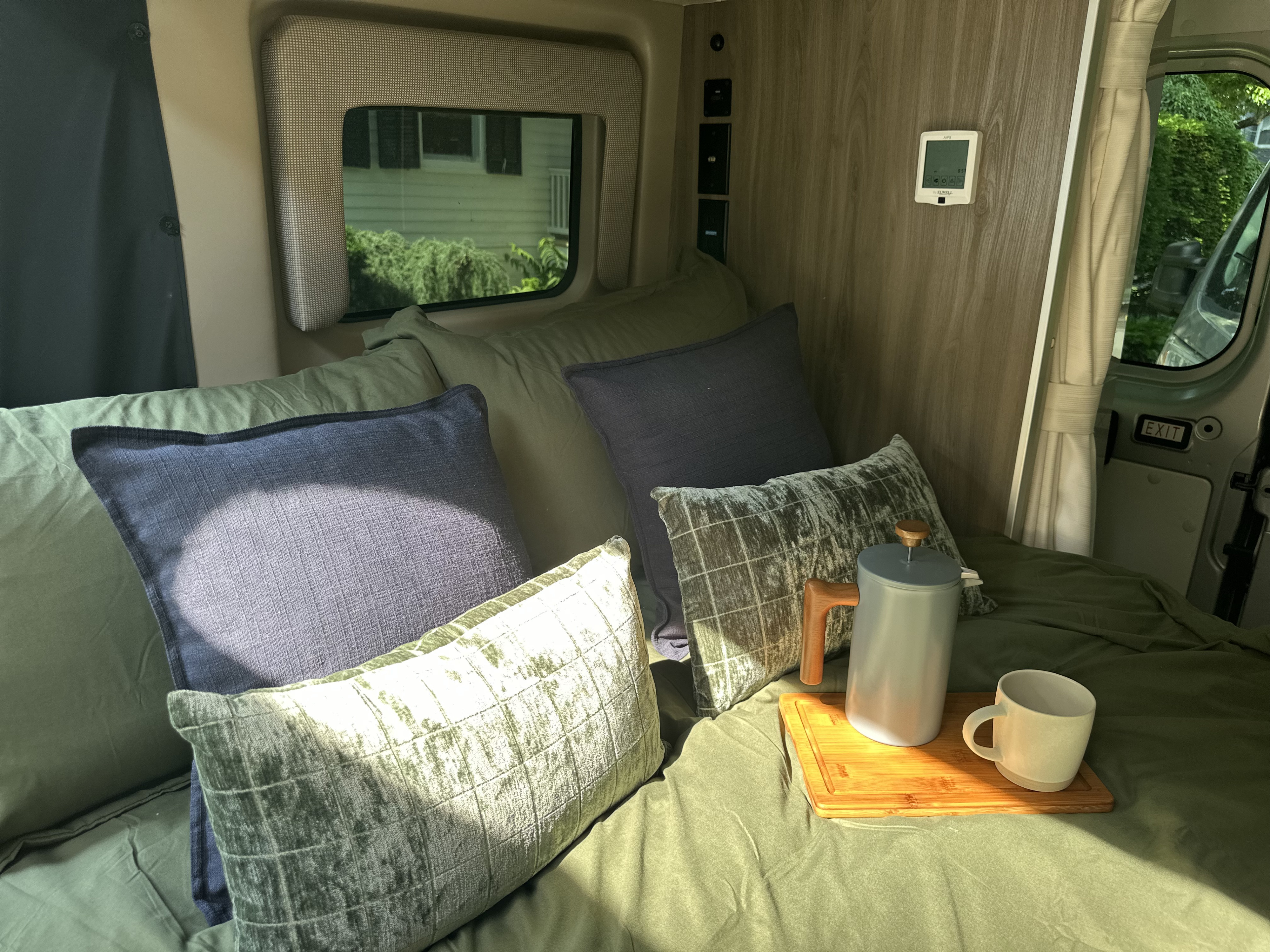 An RV rental's cozy bed with green sheets, blue & green pillows, and a coffee setup on a wooden tray by the window.. Thor Motor Coach Rize 18G pop top 2024