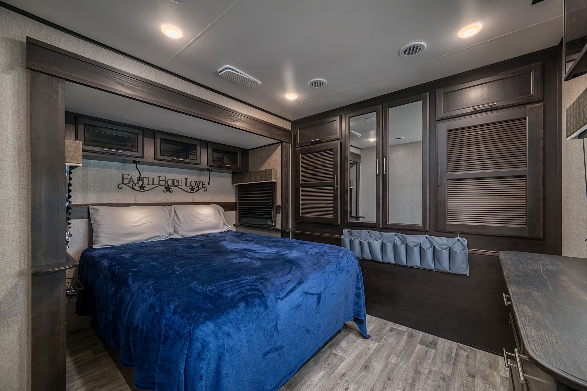Cozy RV rental bedroom features a plush bed, "Faith Hope Love" decor, and ample dark wood storage cabinets.. Jayco Eagle 2020