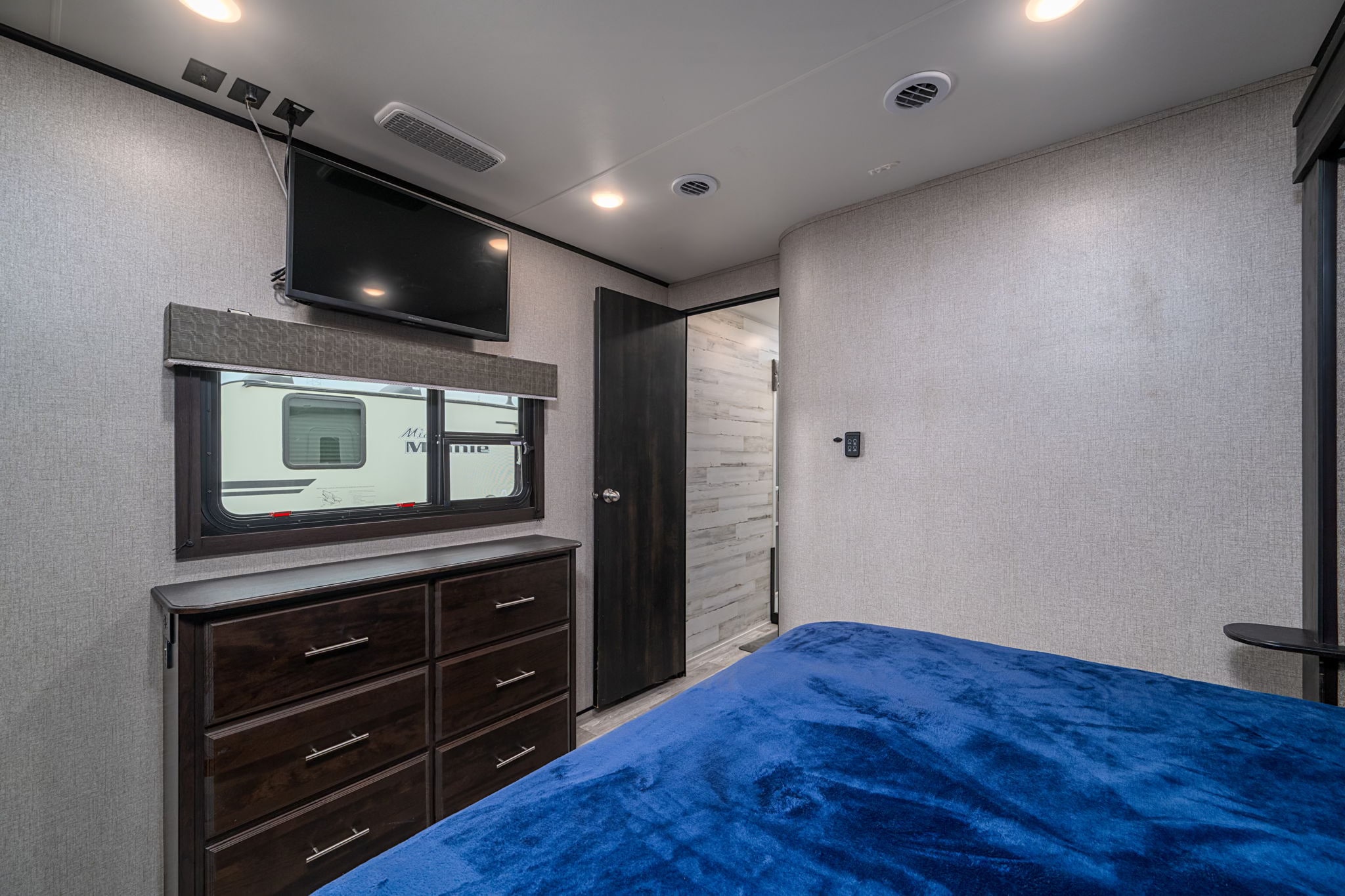 Interior of an RV rental bedroom, showcasing a TV, dresser, window, and inviting blue bed for a cozy stay.. Jayco Eagle 2020