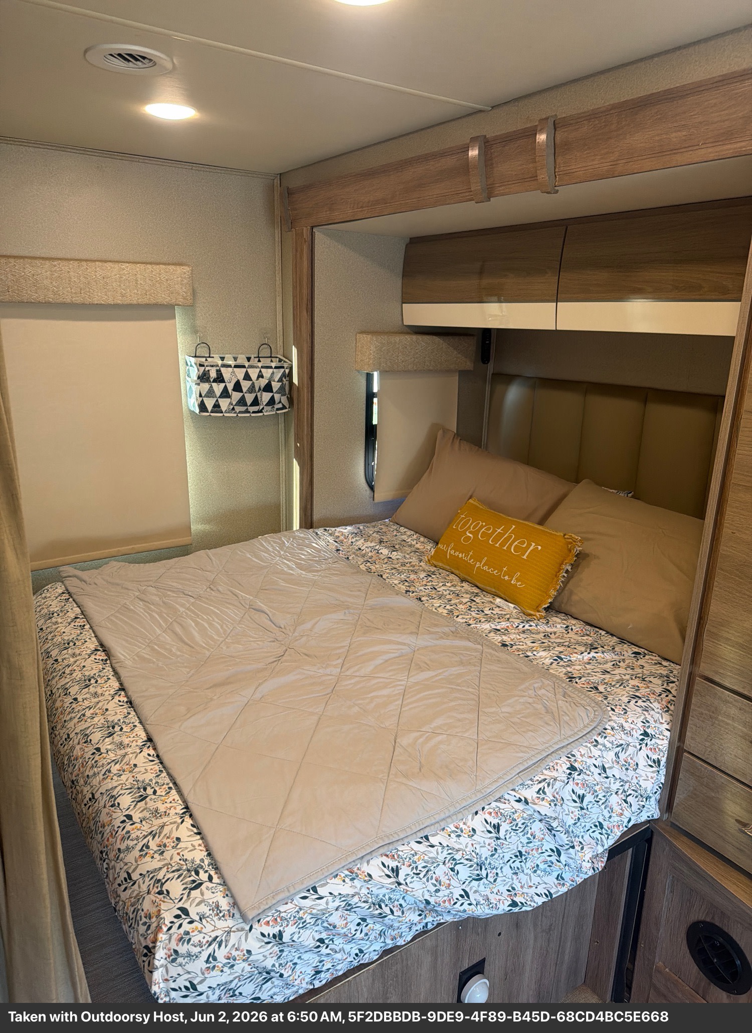 Cozy RV rental bedroom featuring a comfy bed with floral sheets, a yellow "together" pillow, and overhead cabinets.. Entegra Coach Qwest 2020