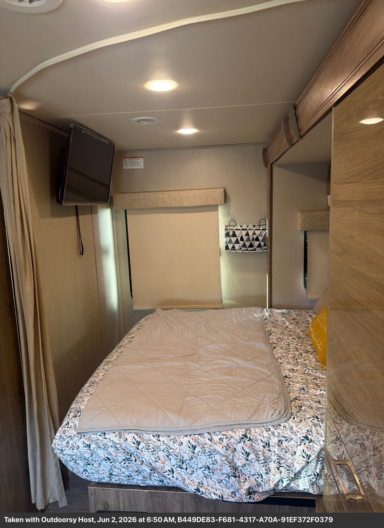 Cozy RV rental bedroom with a comfortable bed, floral sheets, TV, and overhead lighting, perfect for your next adventure.. Entegra Coach Qwest 2020