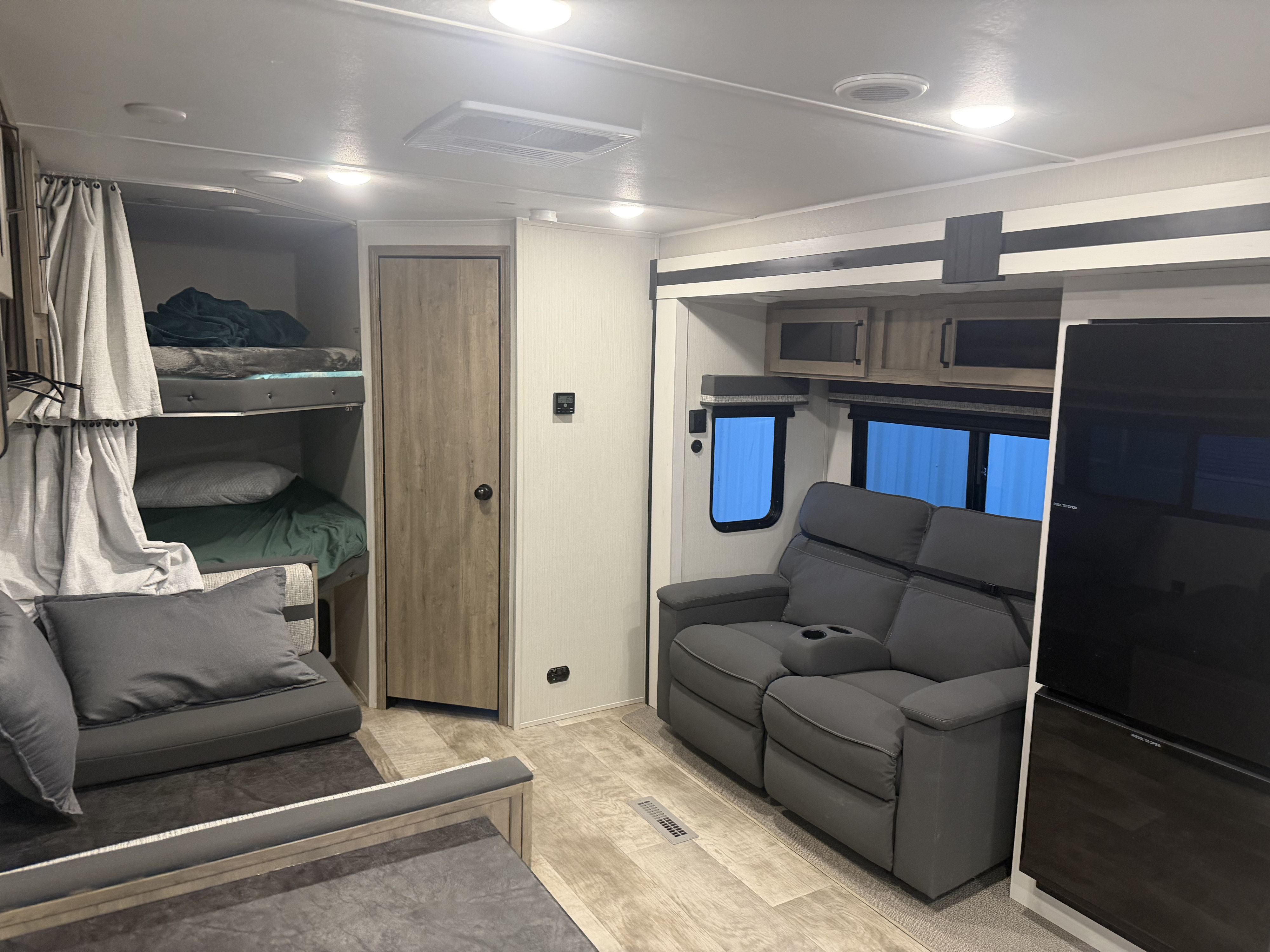 An RV rental's inviting interior: bunk beds with privacy curtains, gray recliners, and a TV unit define the living space.. Forest River Palomino Puma 2024
