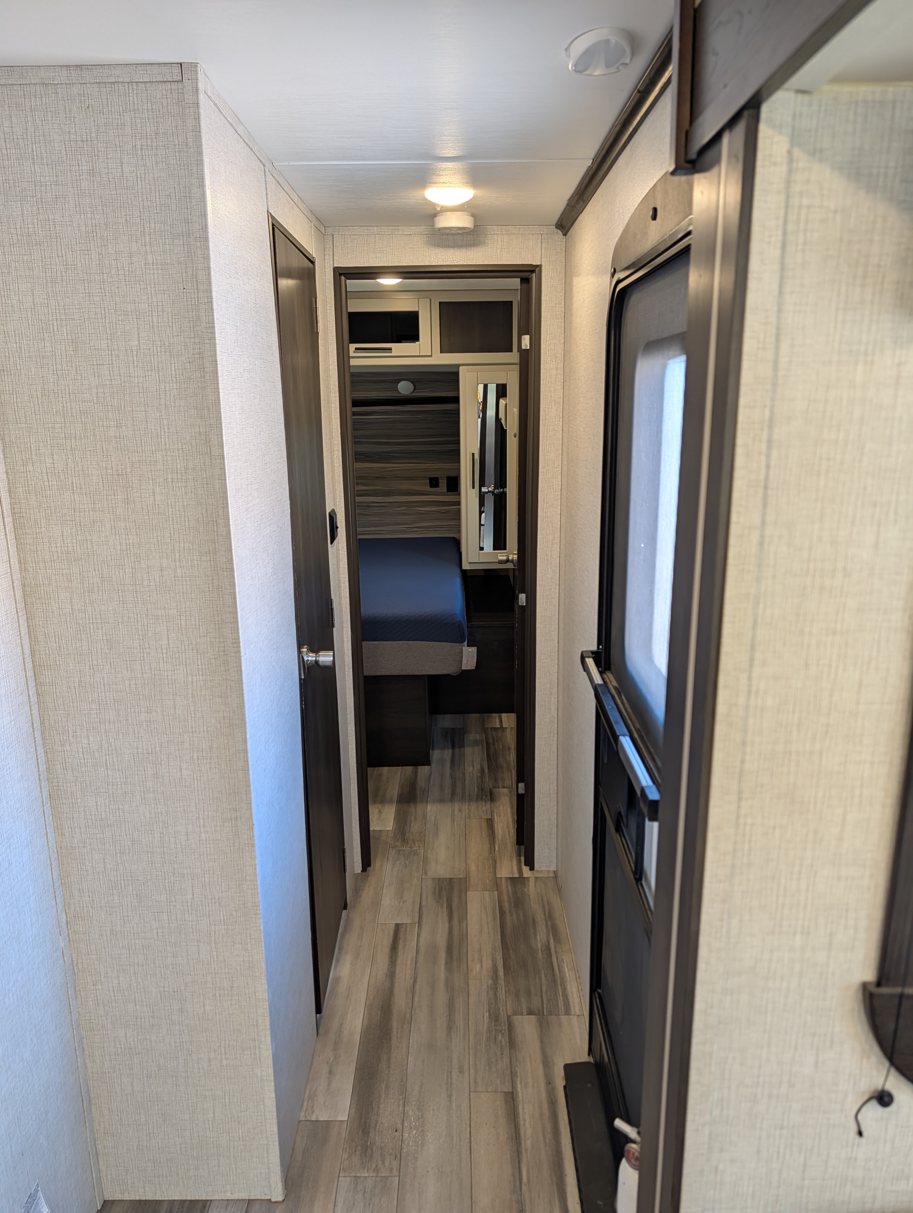 RV rental: View of a modern RV interior hallway with wood-look floor, leading to a bedroom with a blue bed and mirrored closet.. Crossroads RV Cruiser Aire 2022