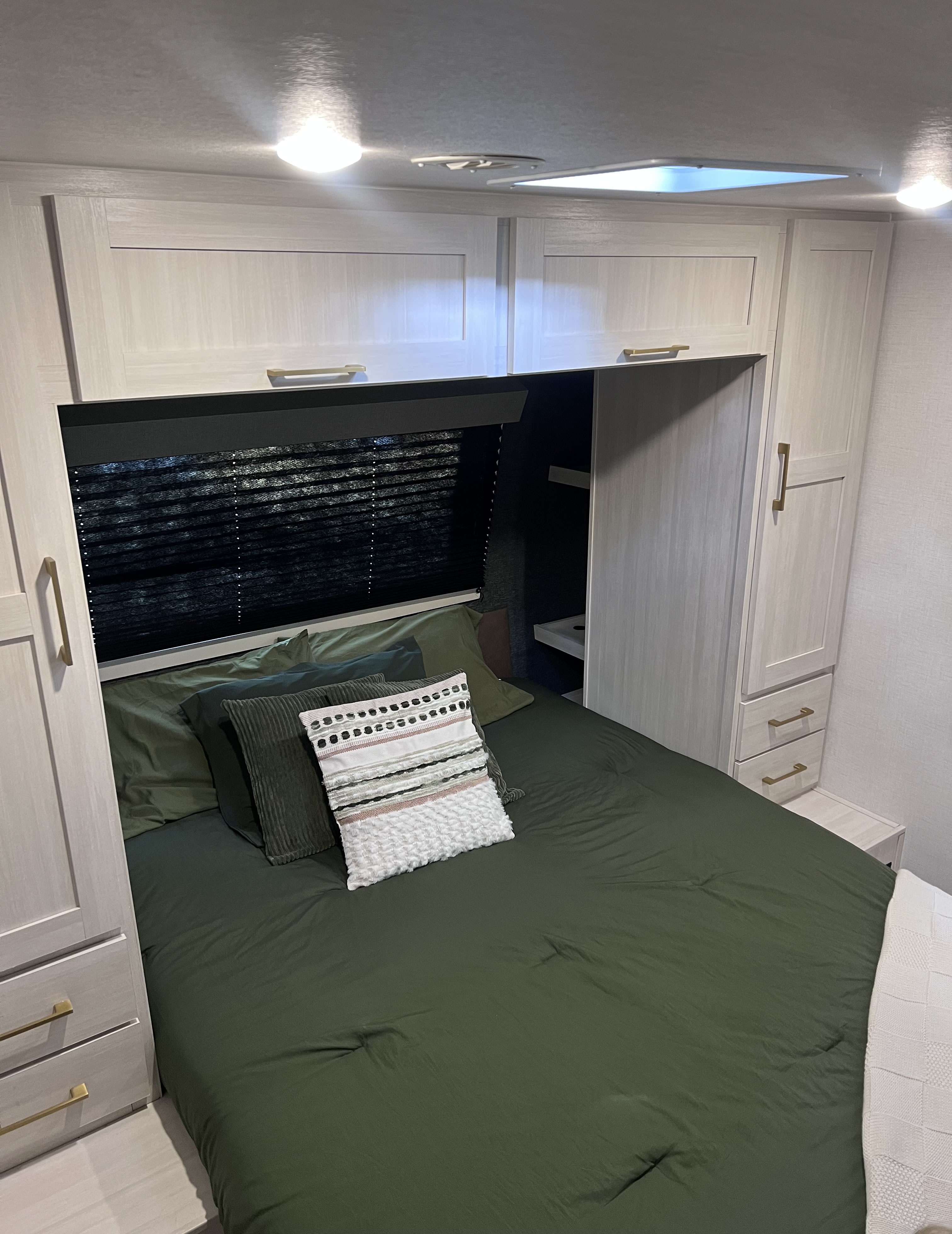 Cozy RV rental bedroom: olive green bed, light wood cabinets with gold handles, window blinds, and built-in storage above.. Forest River Surveyor Legend 2026