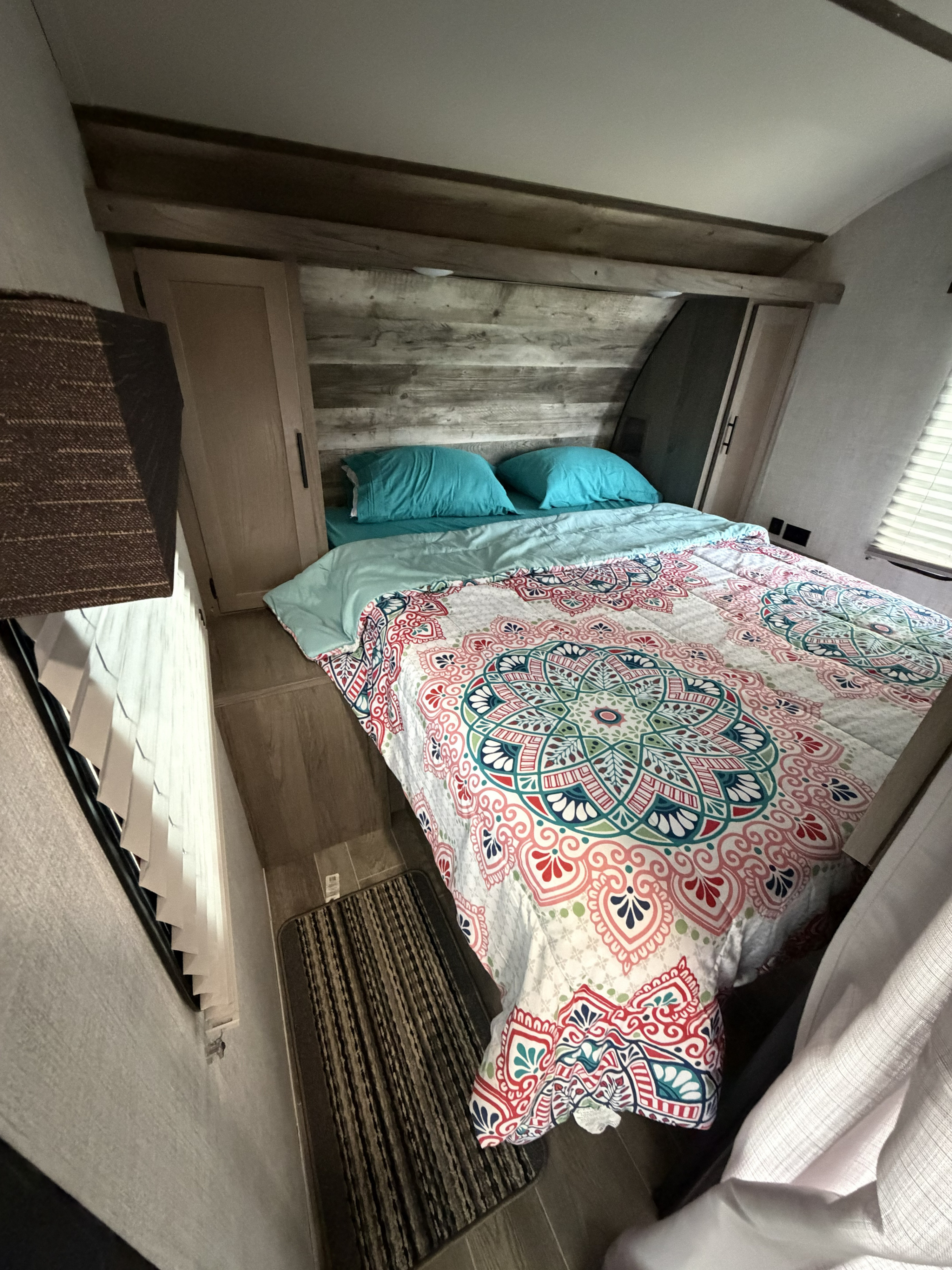 Cozy RV rental bedroom with a vibrant mandala comforter, light blue pillows, wood headboard, and small cabinets.. Gulf Stream Ameri-Lite 2021